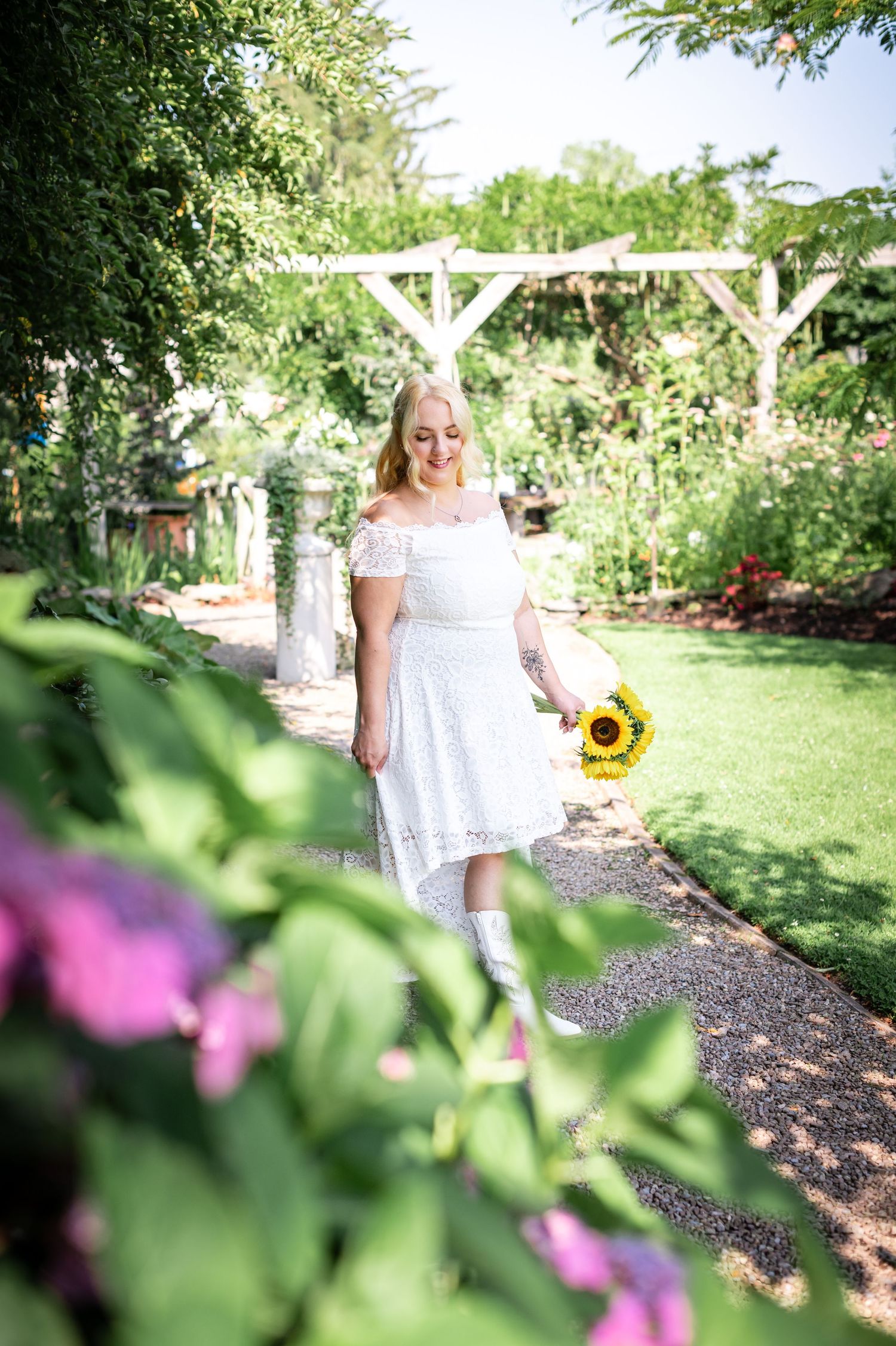 Summer garden portrait with person holding sunflower amid blooming flowers.