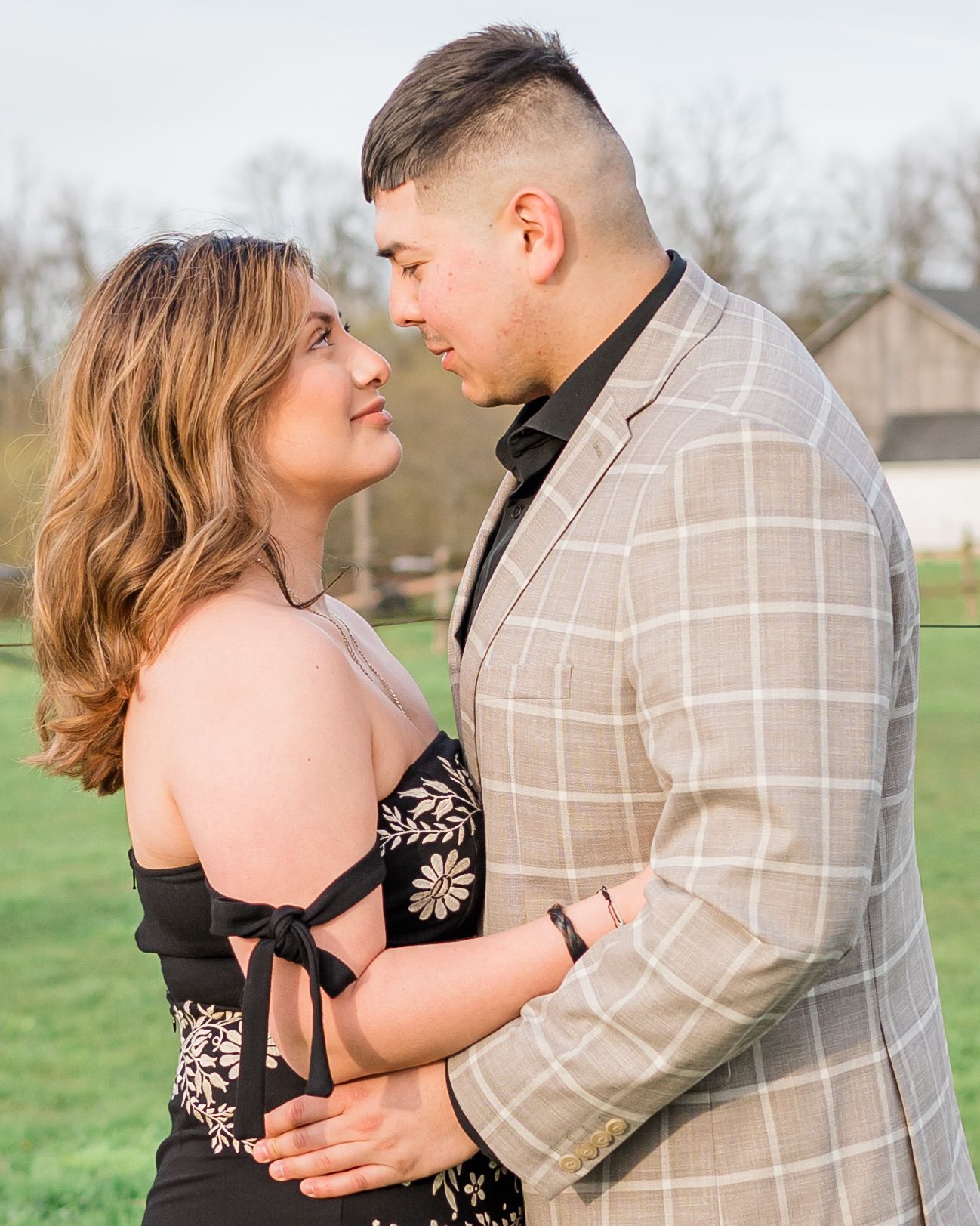 A romantic couple embraces in formal attire outdoors on a grassy lawn.