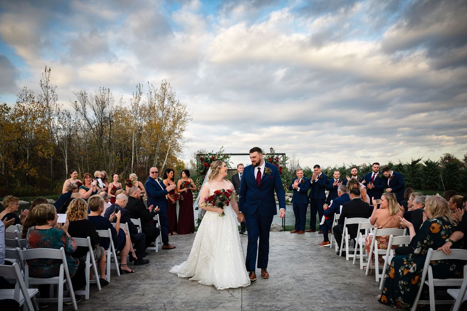 Wedding ceremony guests cheer as a couple walks down the outdoor aisle.