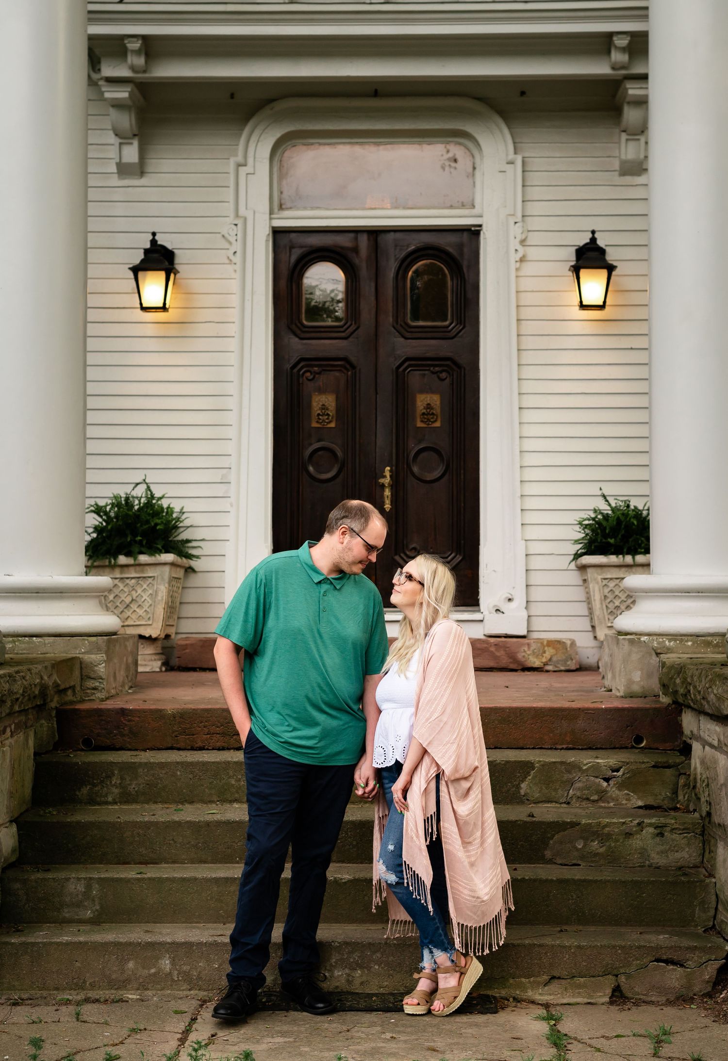 Couple stands on steps of elegant white colonial building with lanterns.