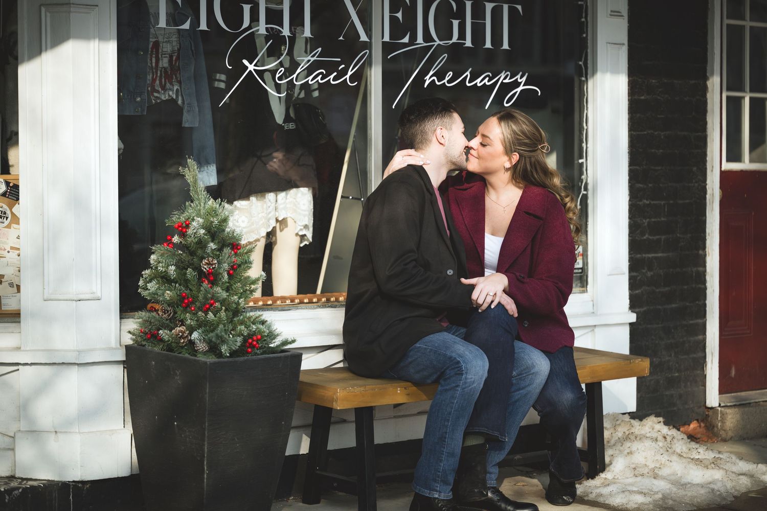 A couple shares an intimate moment together on a porch with white columns and red flowers in the background.