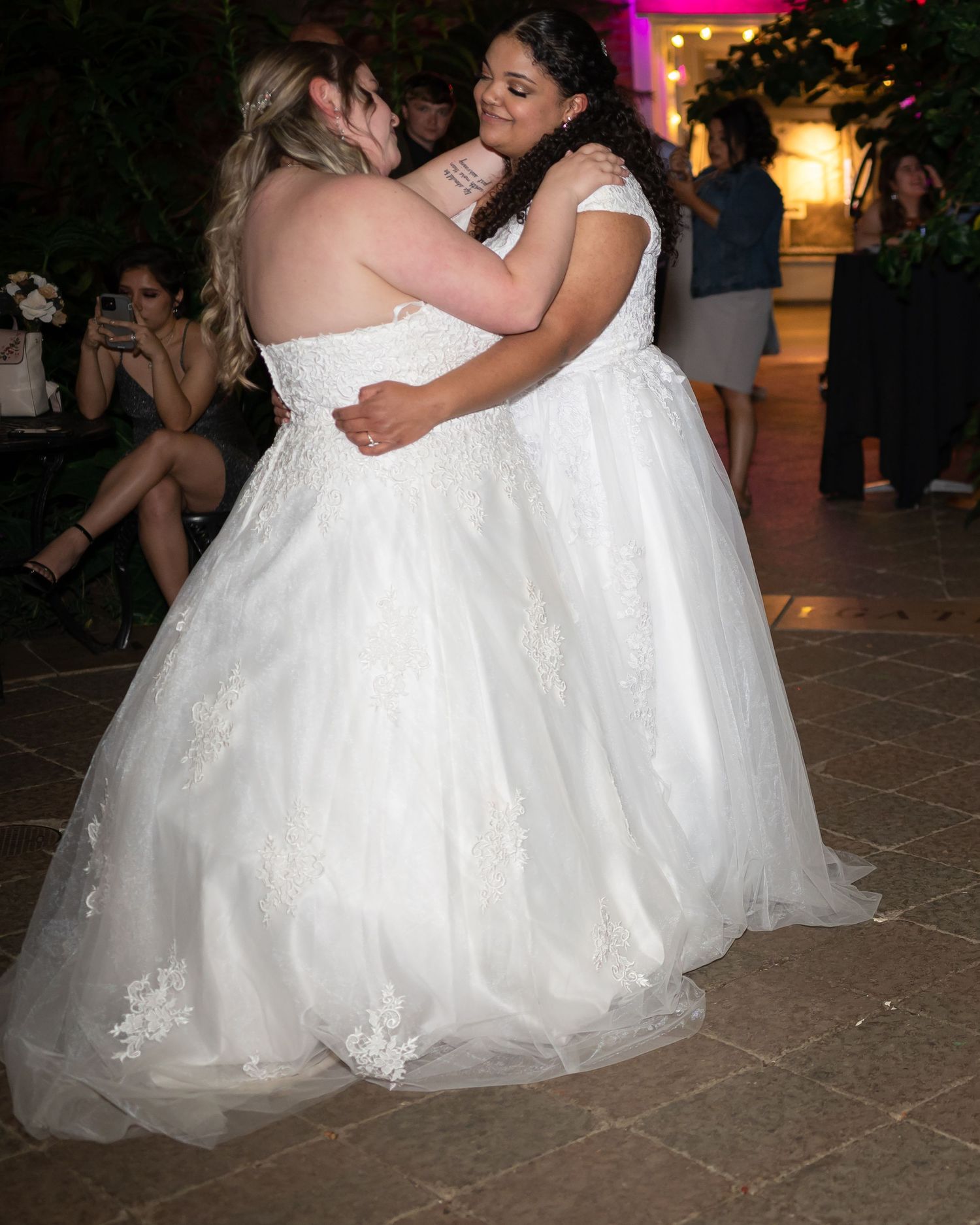 Two brides in flowing white gowns share a dance together during their wedding reception.