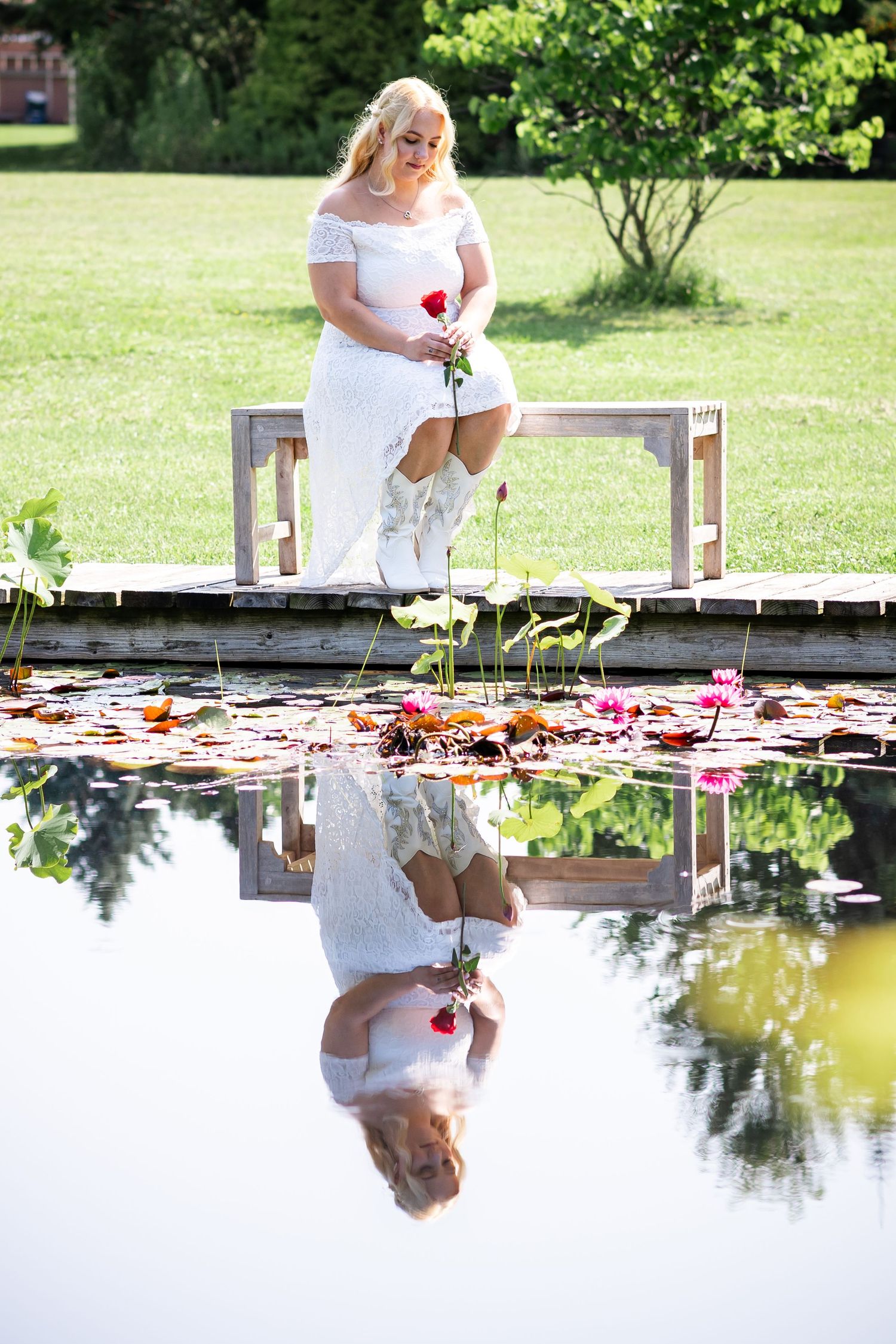White dress reflecting in a pond with lily pads and flowers at a garden.