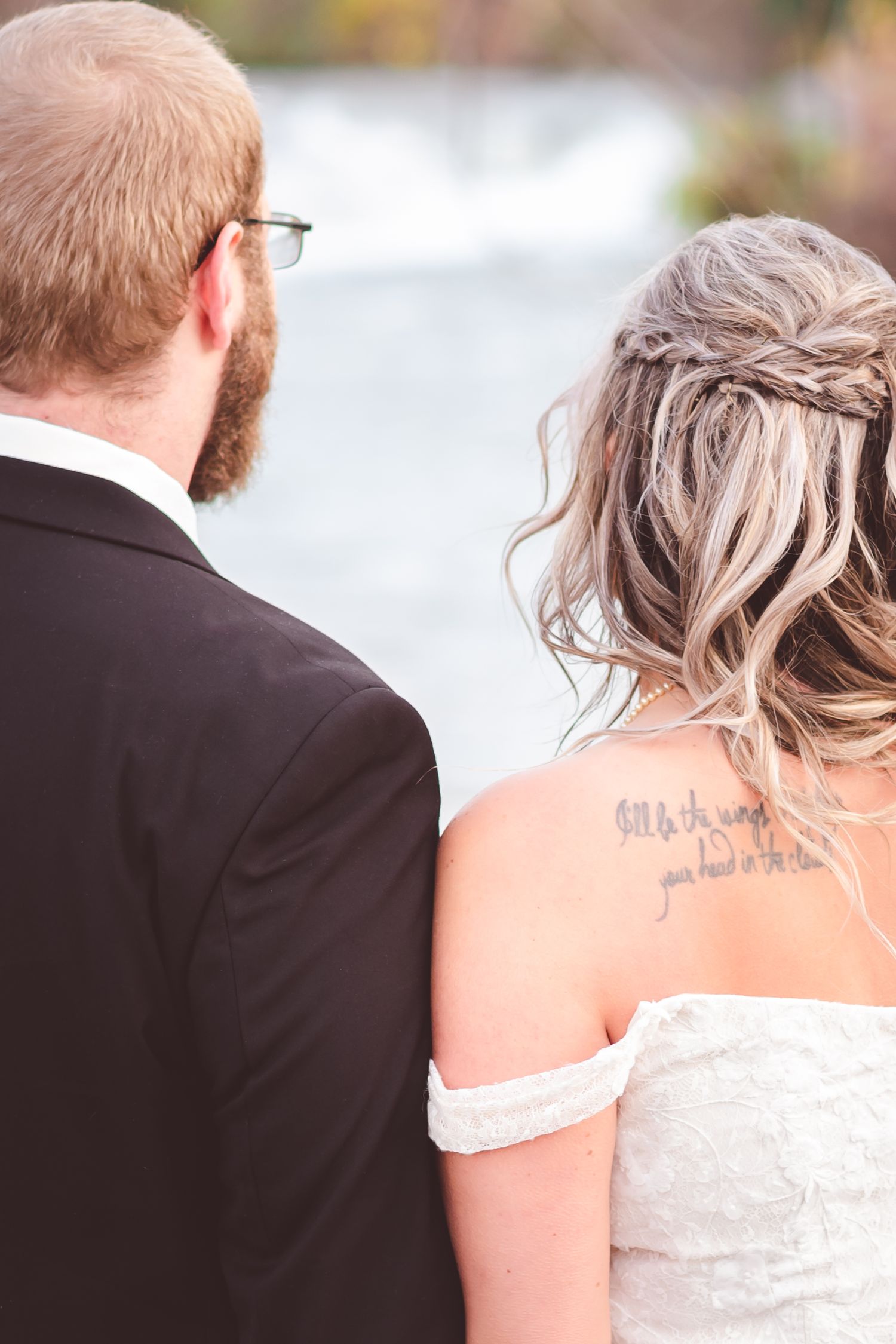 Close-up view of wedding couple from behind looking out at waterfall scenery.