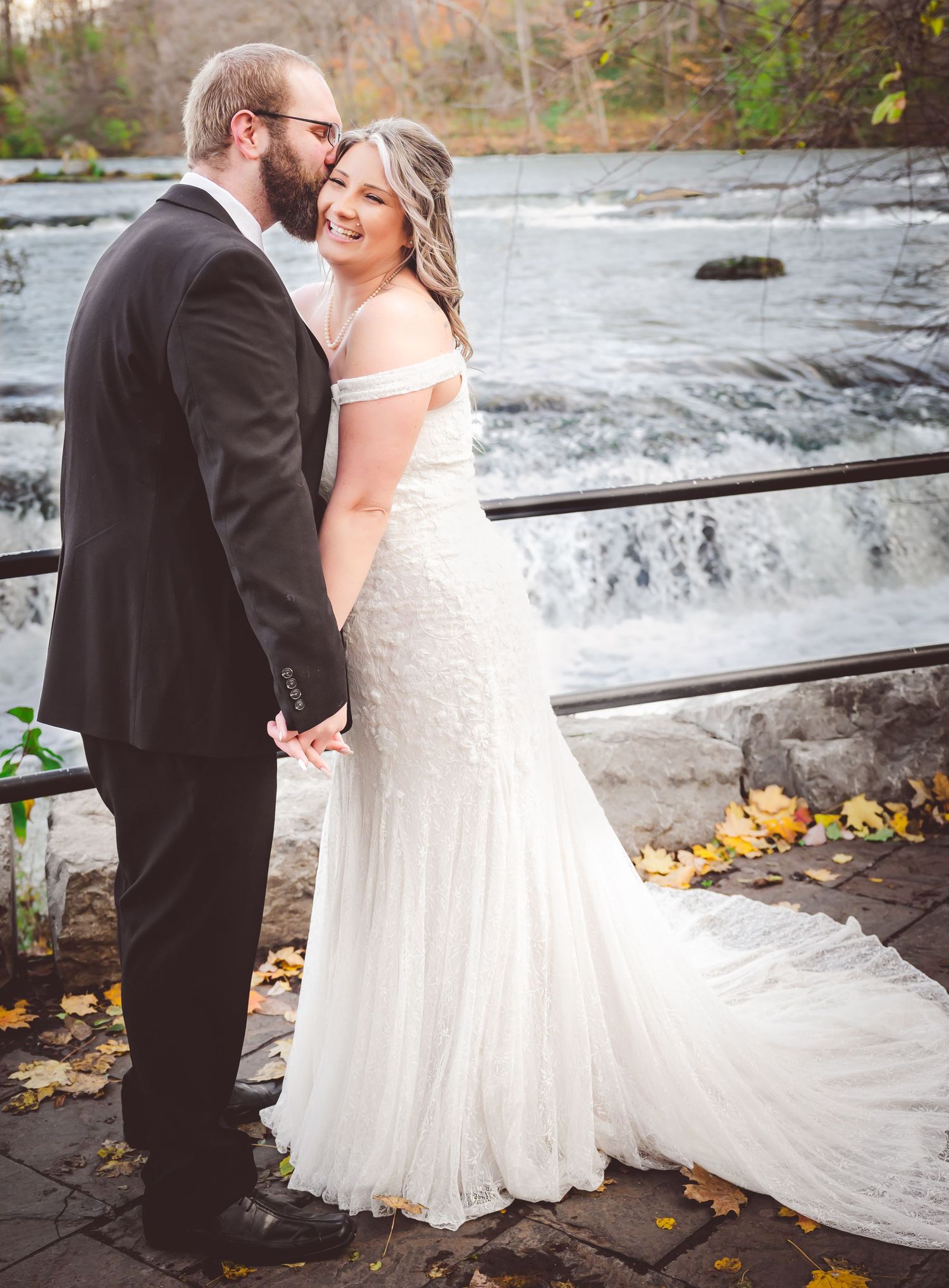 Elegant wedding couple shares intimate moment by cascading waterfall on stone observation deck.