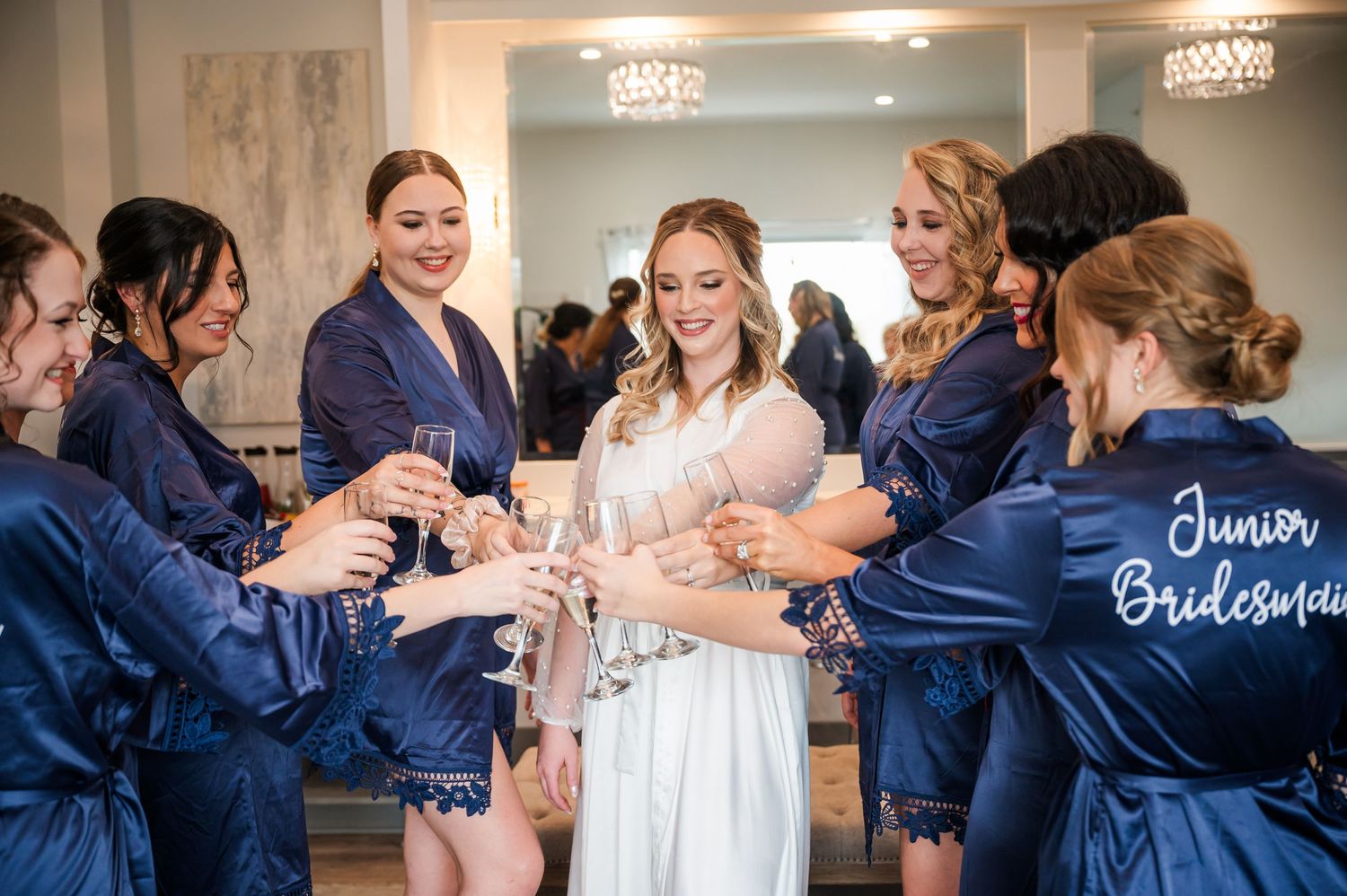 A wedding party in navy blue and blush pink dresses celebrates together in a joyful group dance moment.