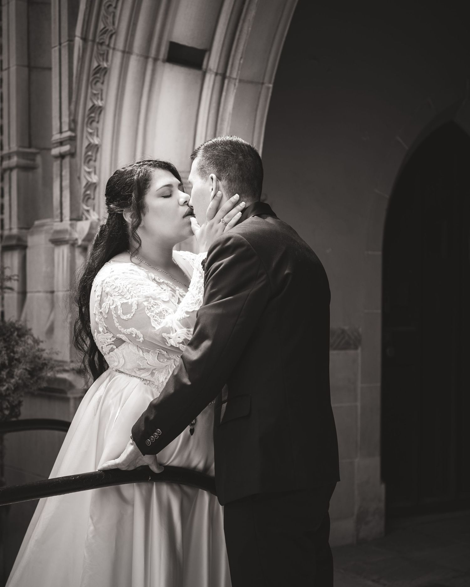 An intimate black and white wedding portrait with a couple embracing under an ornate stone archway.