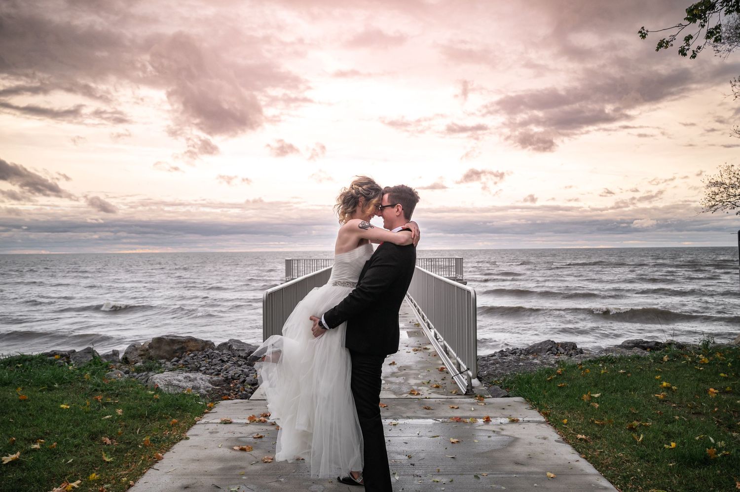 Dramatic sunset wedding portrait on concrete pier overlooking stormy lake.