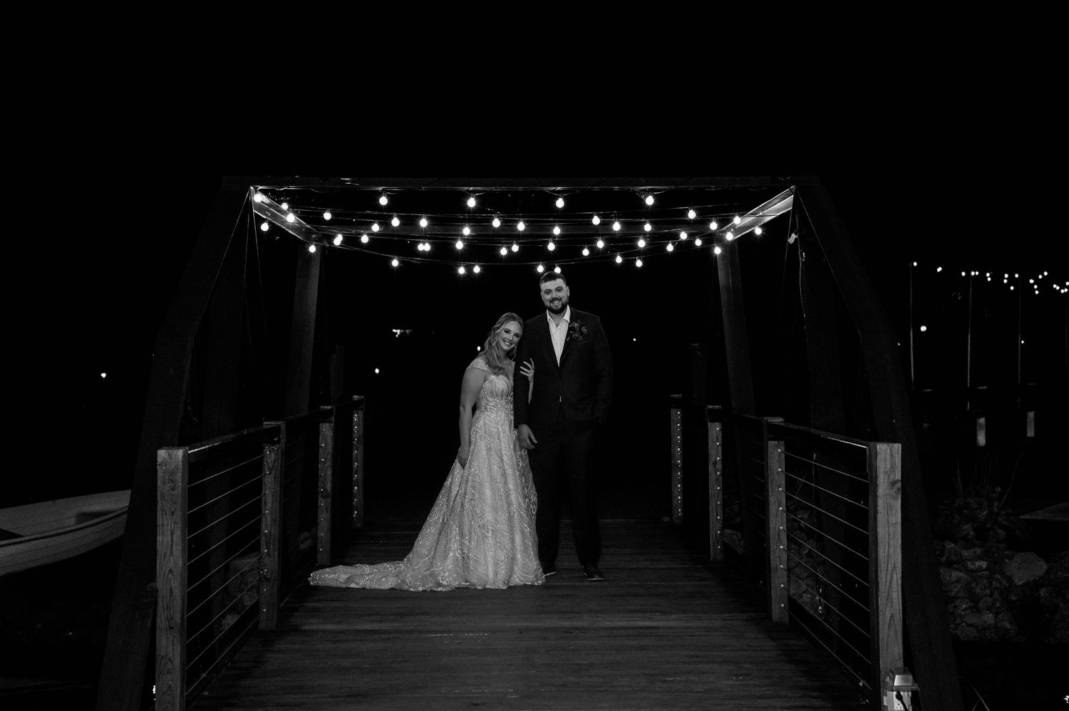 Black and white wedding photo on illuminated bridge deck at night.
