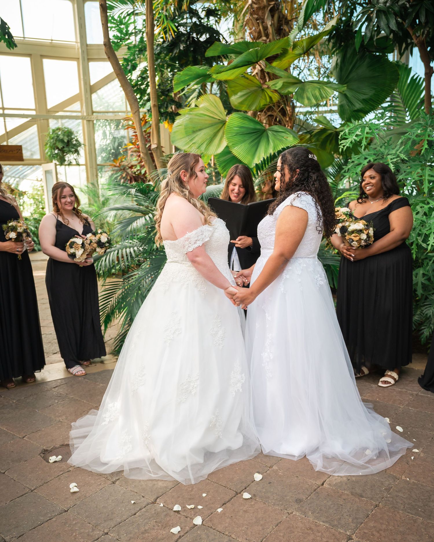 Wedding ceremony in a greenhouse conservatory with attendants in black dresses.