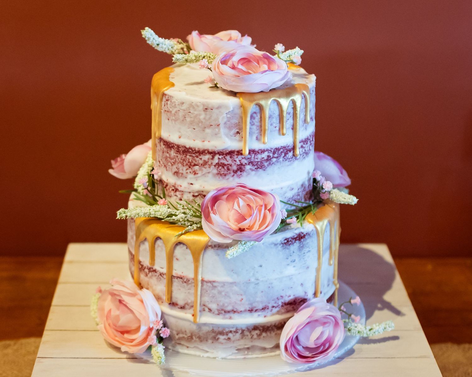 A two-tier wedding cake with dripping icing and fresh pink roses.
