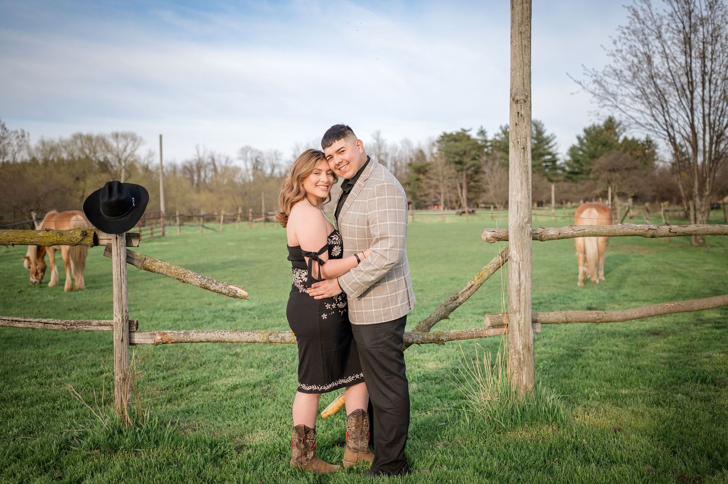 Couple embraces in front of pastoral horse paddock during sunset.