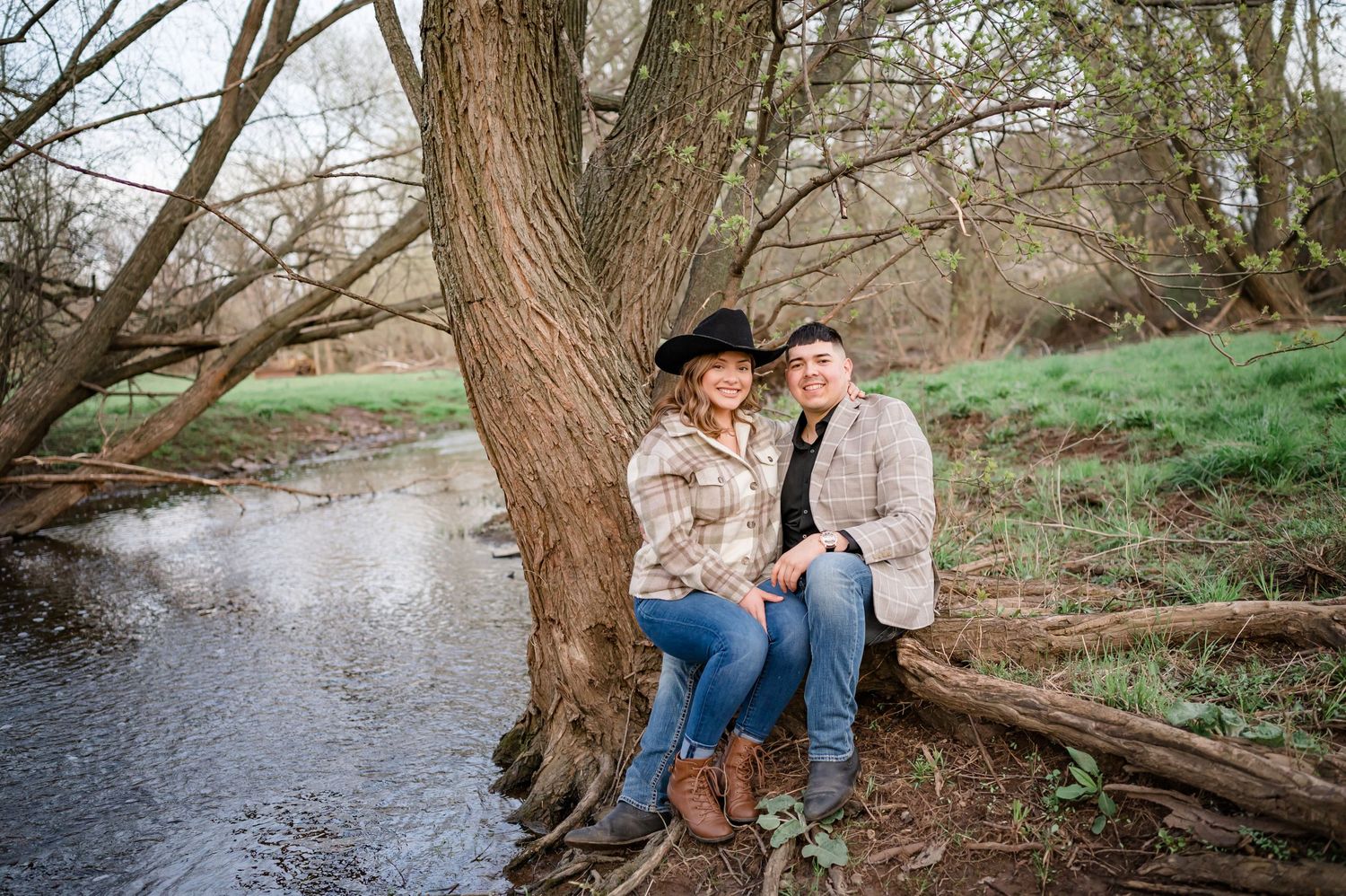 A couple shares a sweet moment while sitting on a fallen tree by a peaceful stream.
