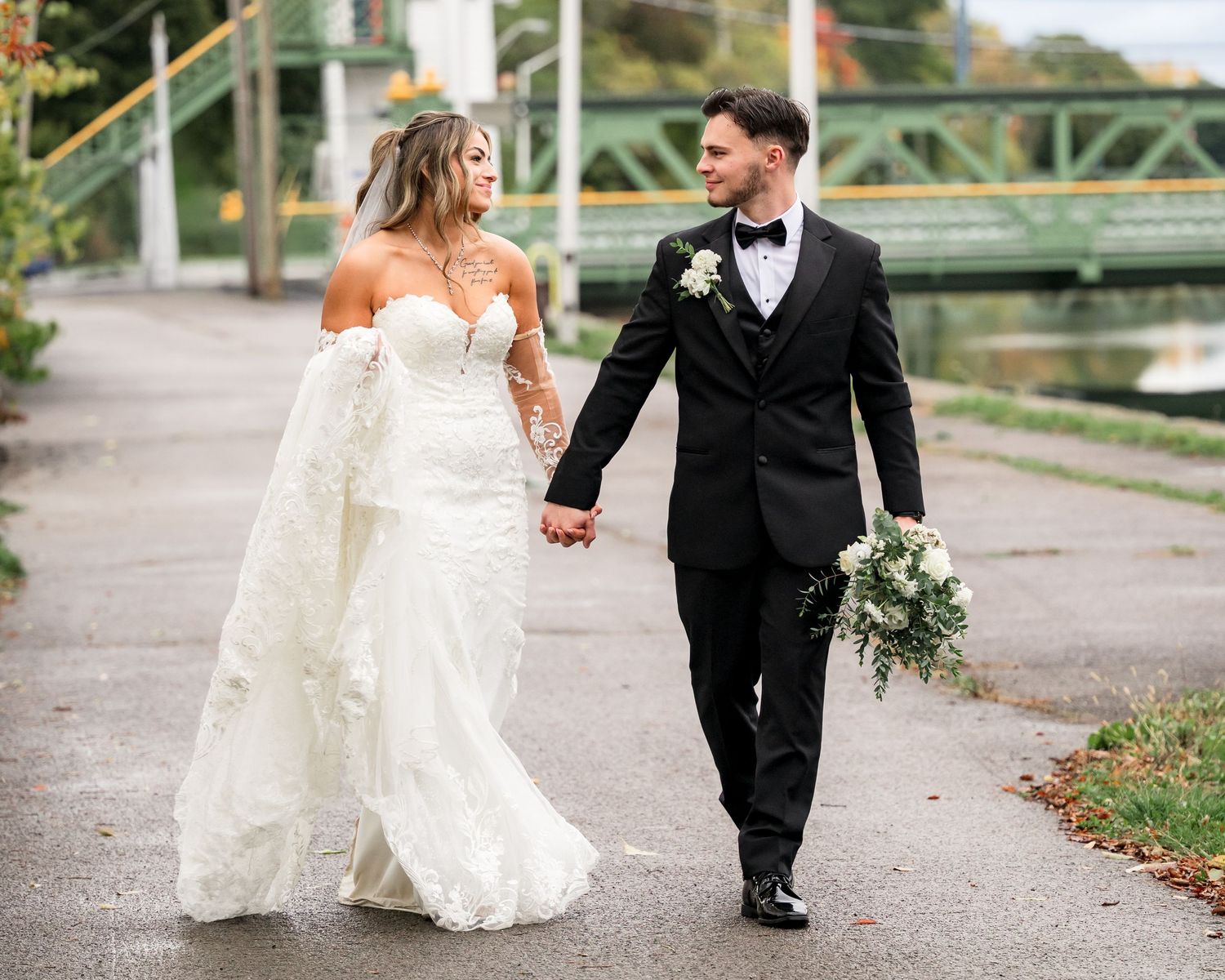 A couple in wedding attire walks together along a path during an autumn day.