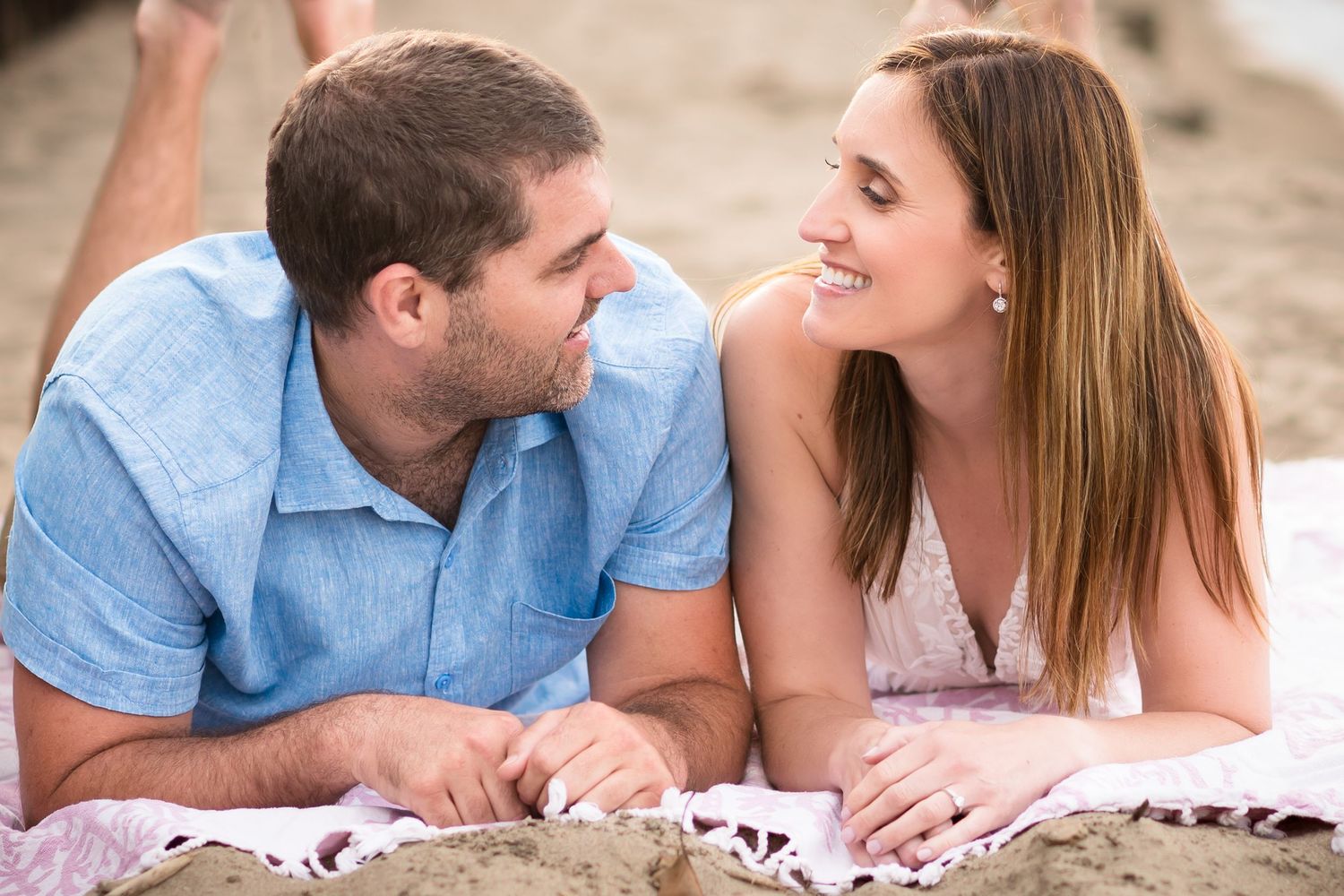 A couple lying on a blanket at the beach sharing a playful moment together.