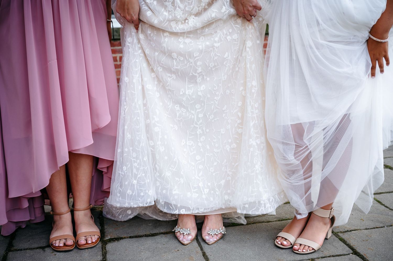 Detail shot of elegant bridal party shoes and dresses in white and pink on stone patio.