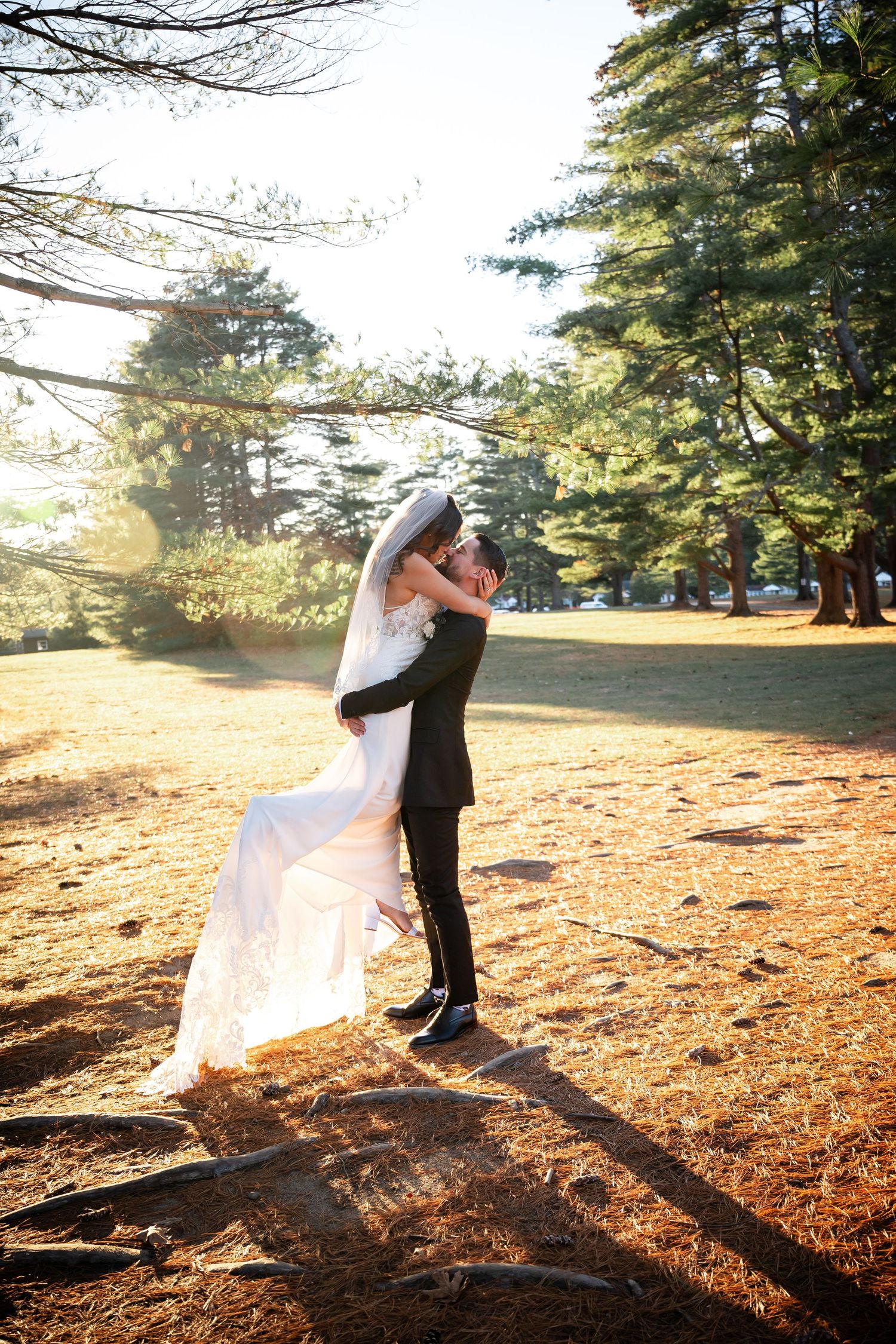 Two people embrace in sunlit forest clearing during romantic outdoor wedding photo session at golden hour.
