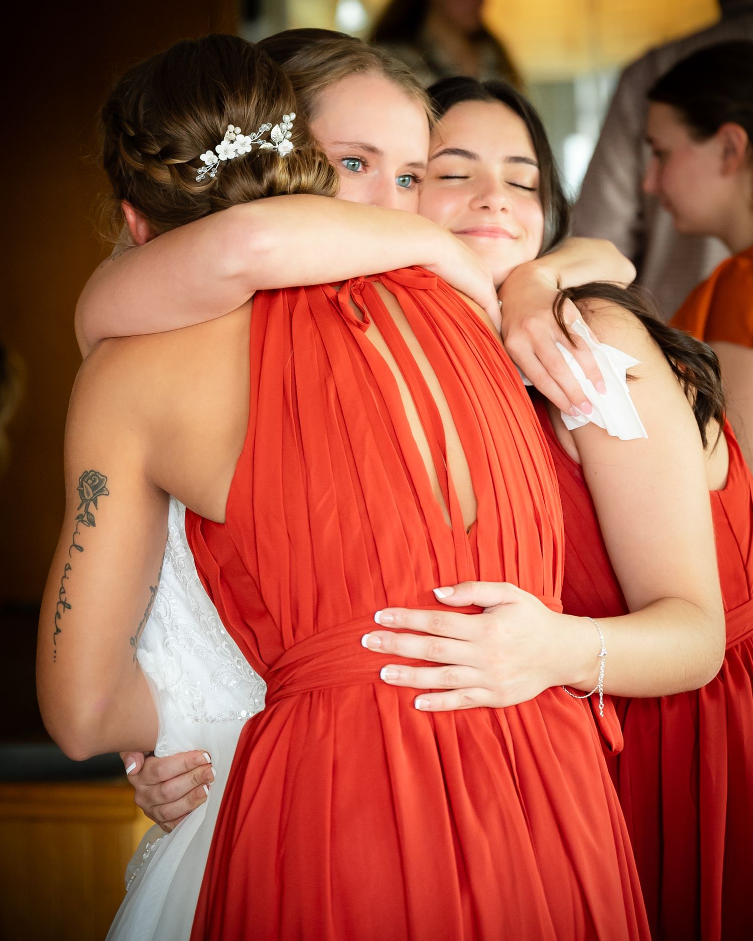 Emotional moment captured as bridesmaids in red dresses share embrace during wedding celebration.