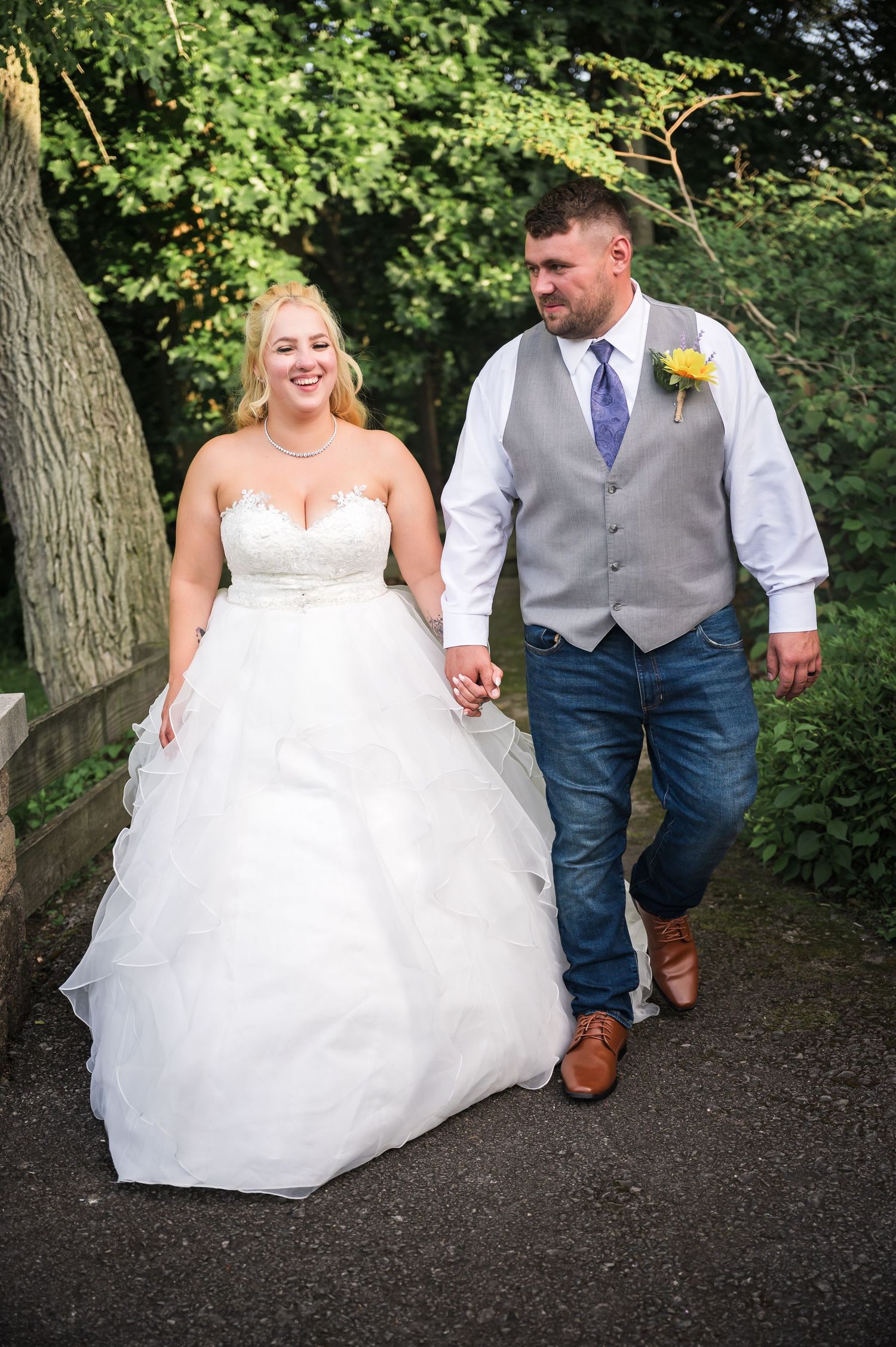 Wedding couple walking hand-in-hand along outdoor path surrounded by greenery.