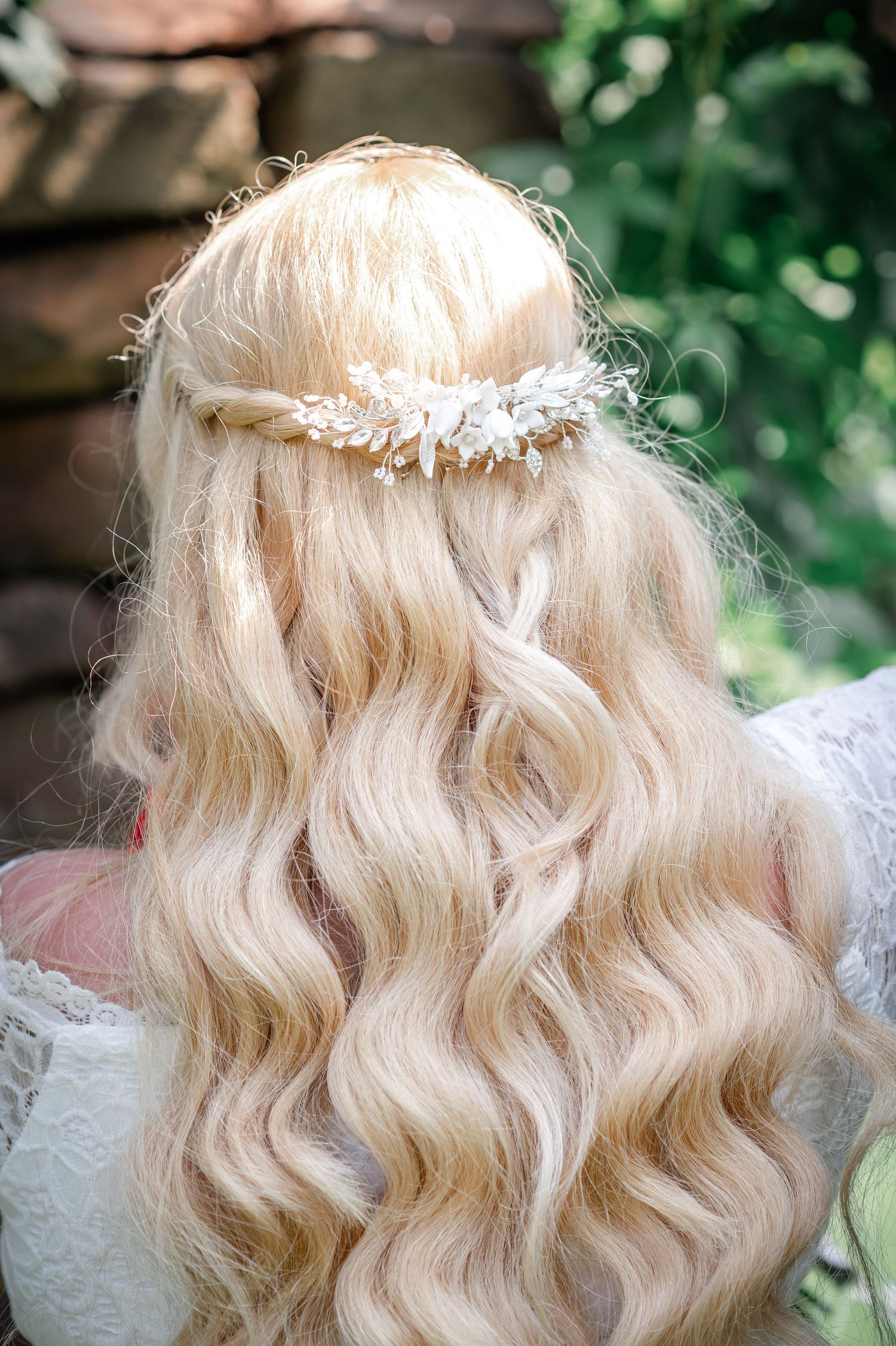 Long blonde wavy hair adorned with a delicate floral headpiece against natural greenery.
