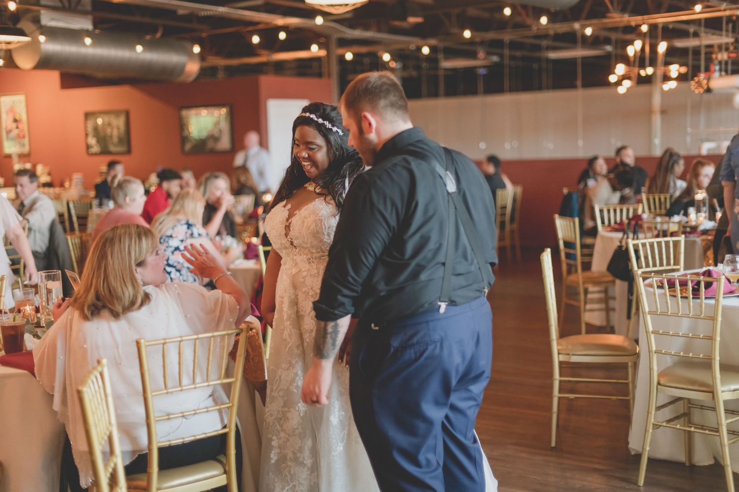 Wedding celebration scene with guests mingling in venue with chandelier lighting.