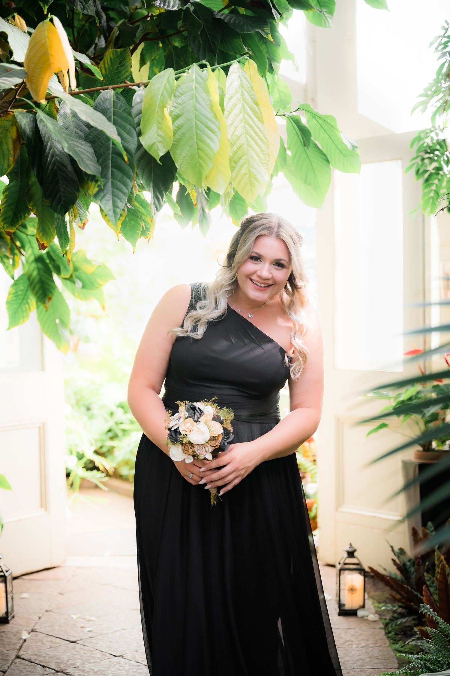 One-shoulder black formal dress in a tropical garden setting with yellow flowers above.