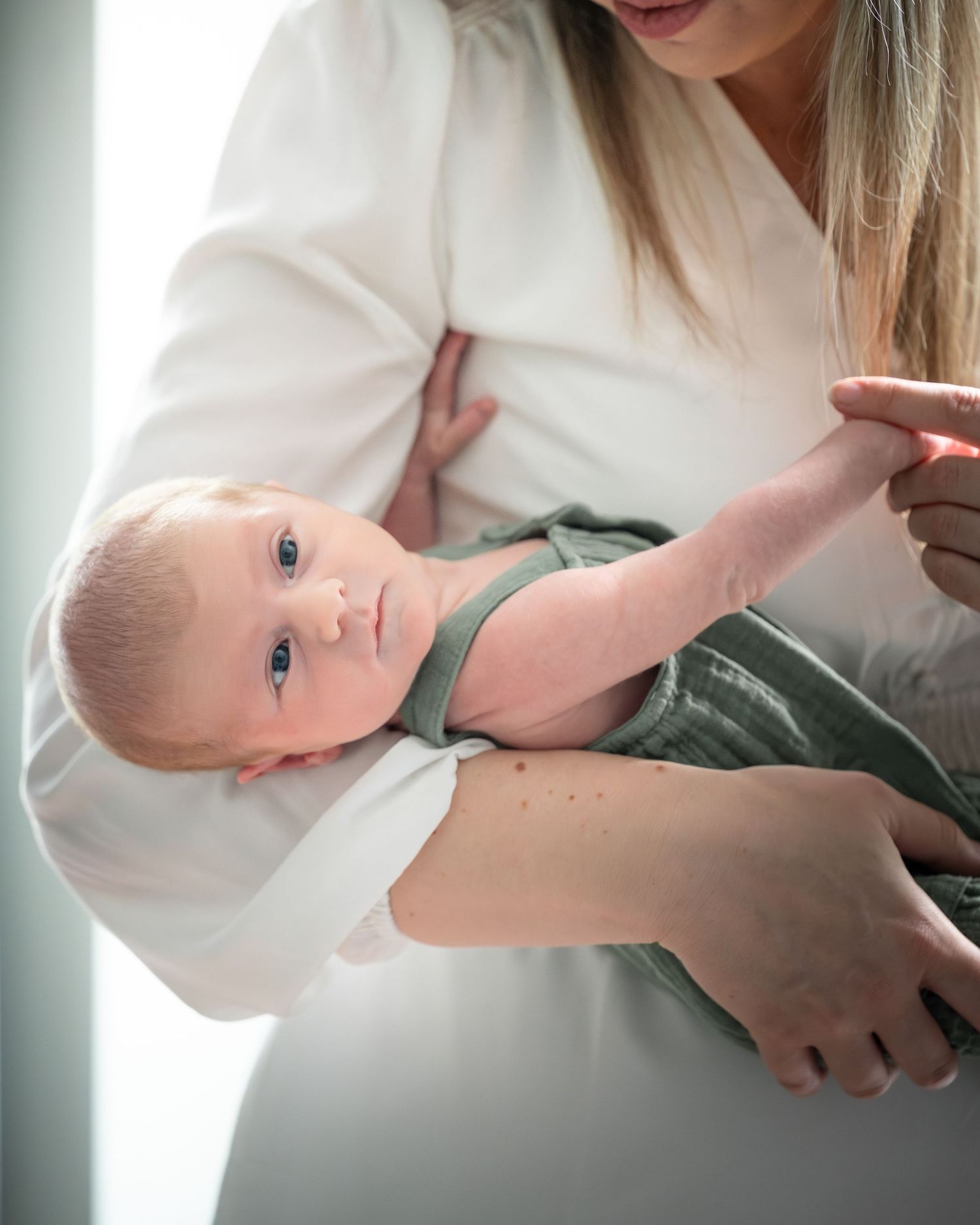 A baby with bright blue eyes lies on their side while being gently held in a caregiver's arms.