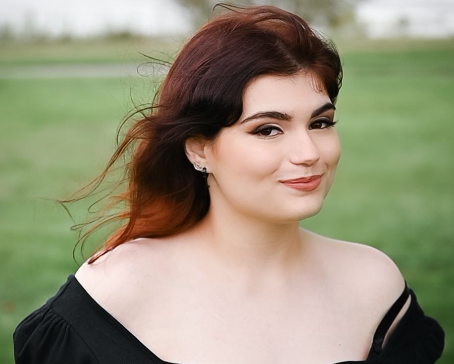 Close-up portrait with swept hair and black off-shoulder dress in outdoor setting.