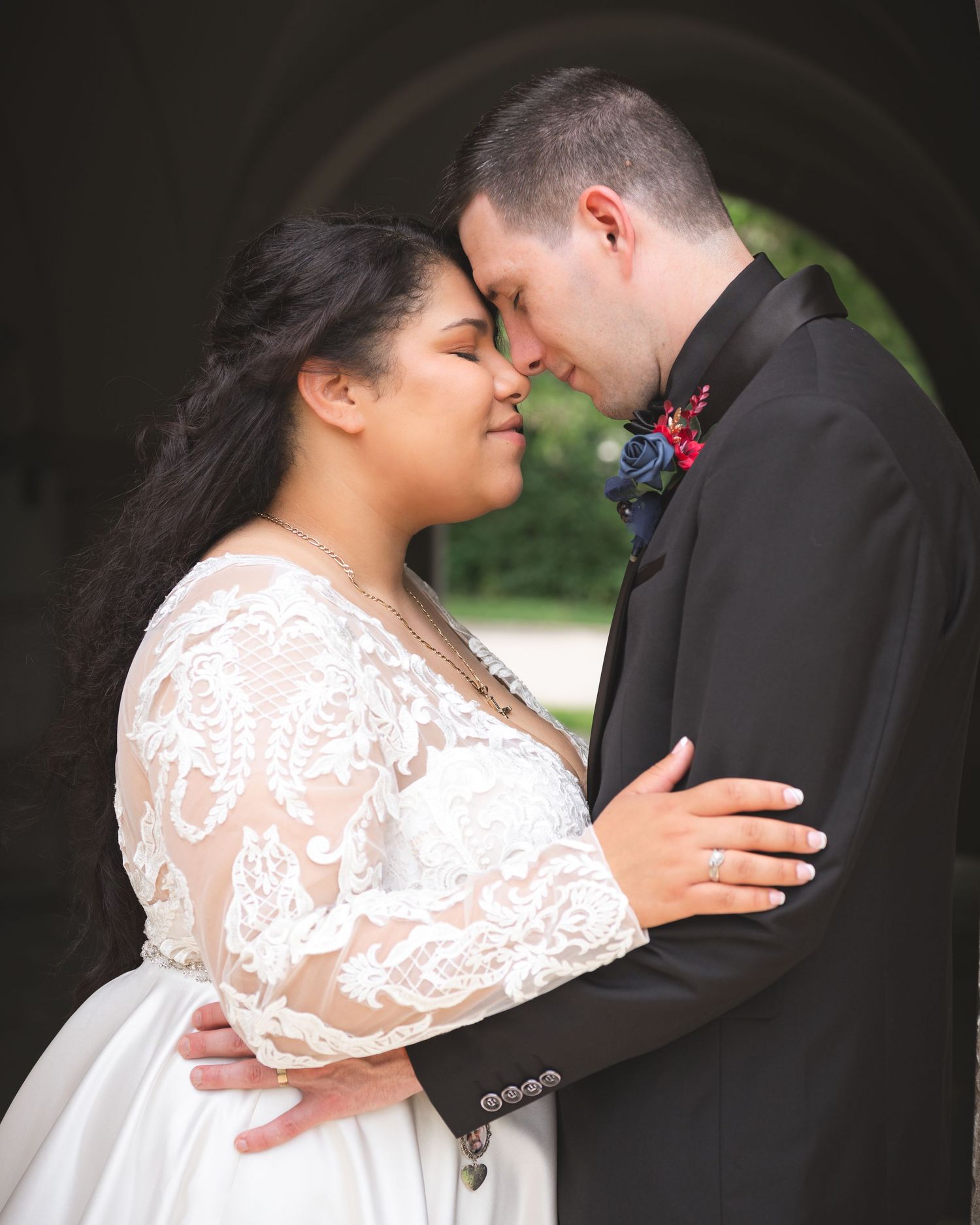 A tender moment between a couple in formal wedding attire standing close together outdoors.