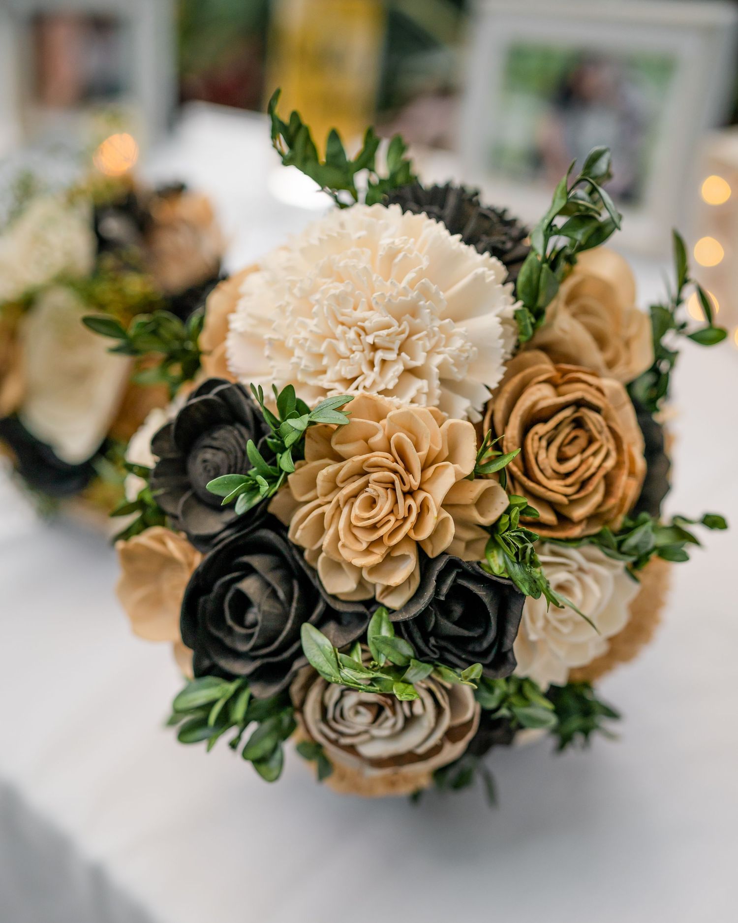 Elegant wedding bouquet featuring cream carnations, beige roses, and dark charcoal flowers with green foliage.