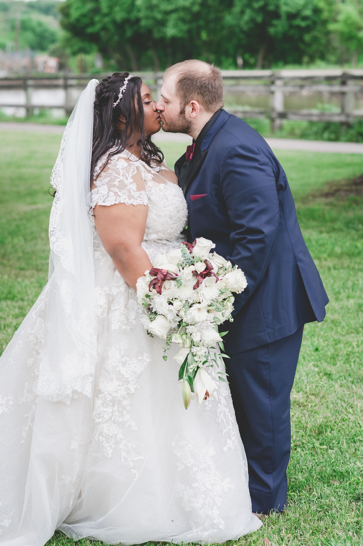 Romantic wedding portrait with white and burgundy bouquet, couple sharing intimate moment outdoors.