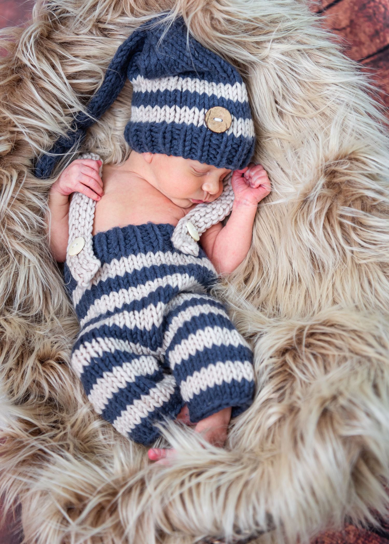 Newborn wearing knitted navy and white striped outfit with matching hat lies on soft furry blanket.