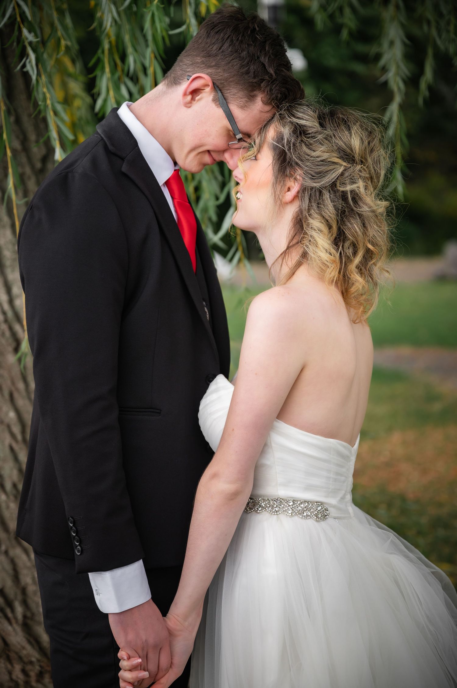 Intimate moment captured under willow tree branches with classic black and white wedding attire.