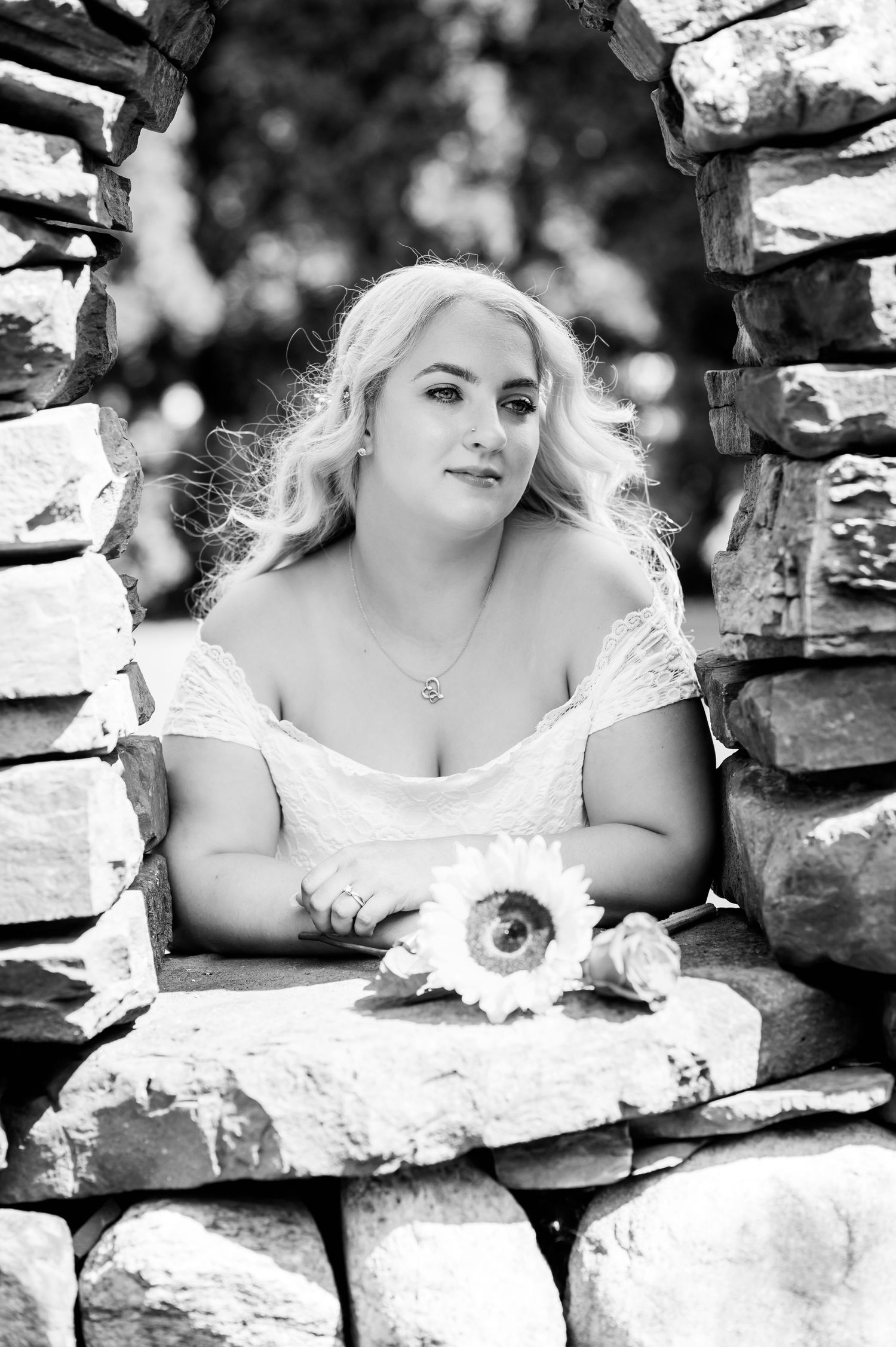 Black and white portrait through stone wall opening with flowers.