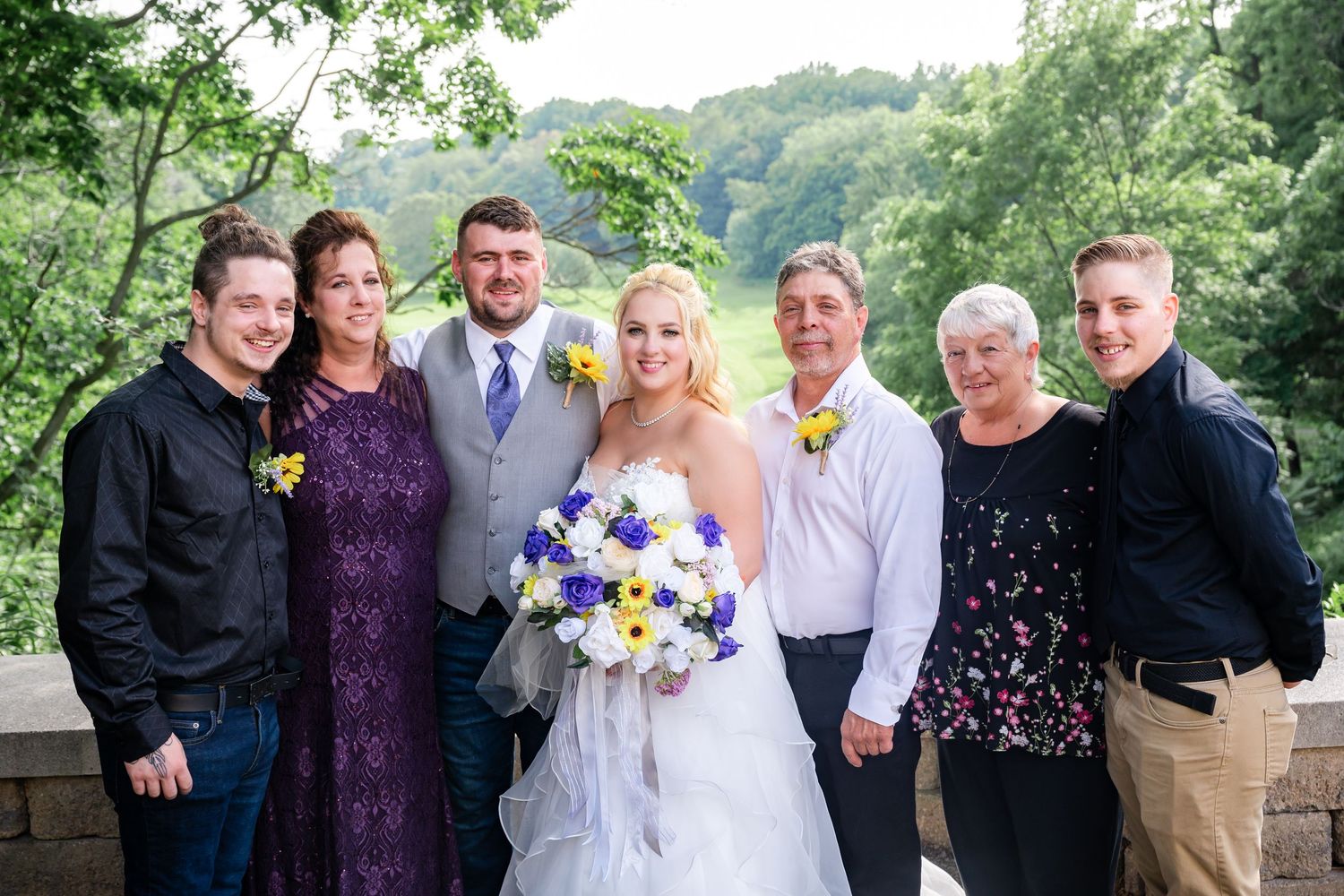 Wedding group photo with family members in formal attire standing together on a scenic overlook.