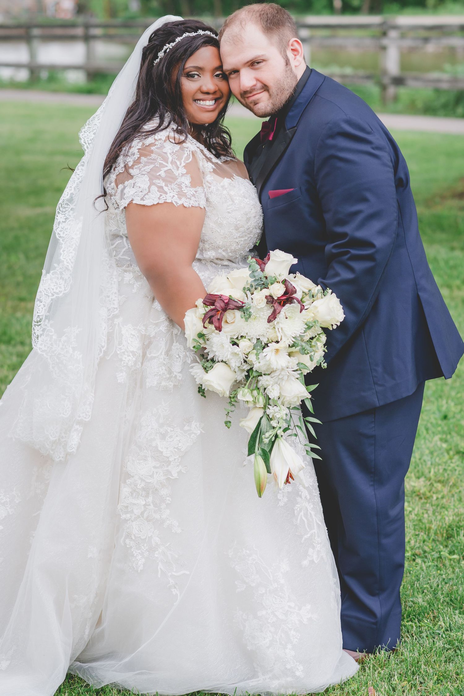 Newlyweds share a loving moment outdoors with elegant white and burgundy bouquet.