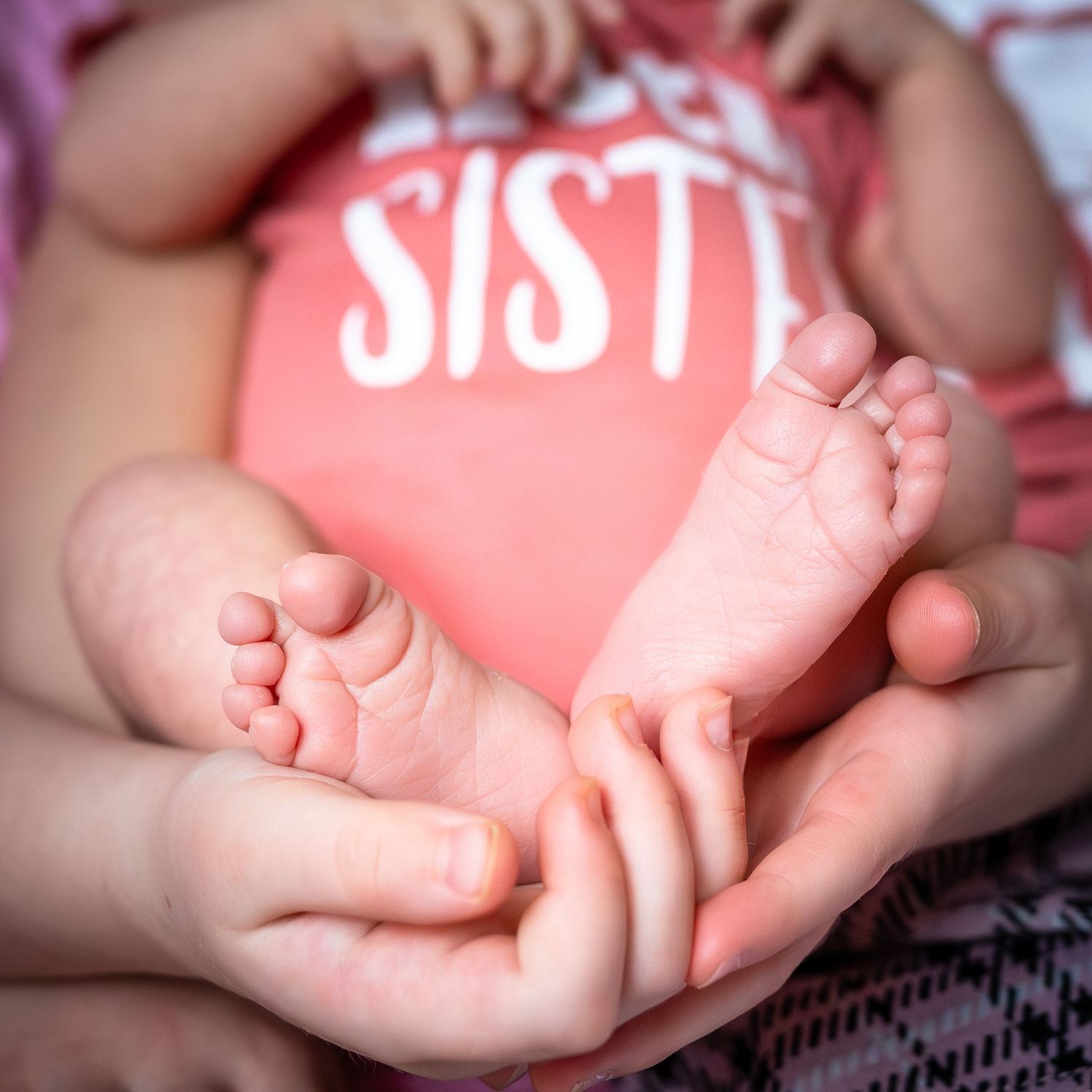 Close-up photo of tiny newborn baby feet being gently held in adult hands against a pink background.