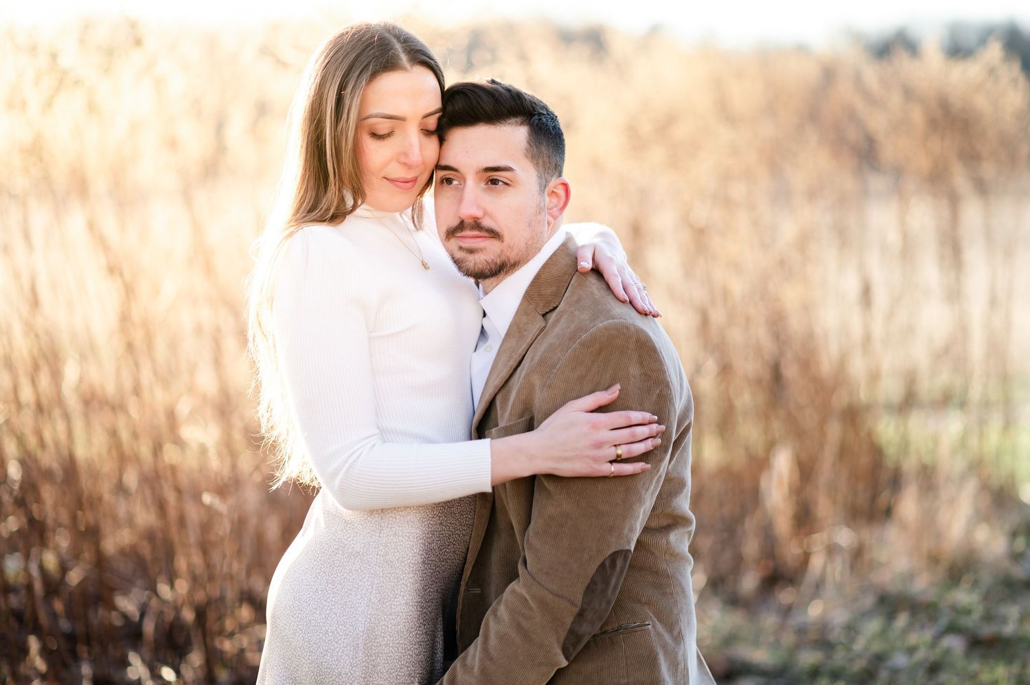 A couple embraces tenderly in a field of tall golden grass during an autumn engagement photoshoot.