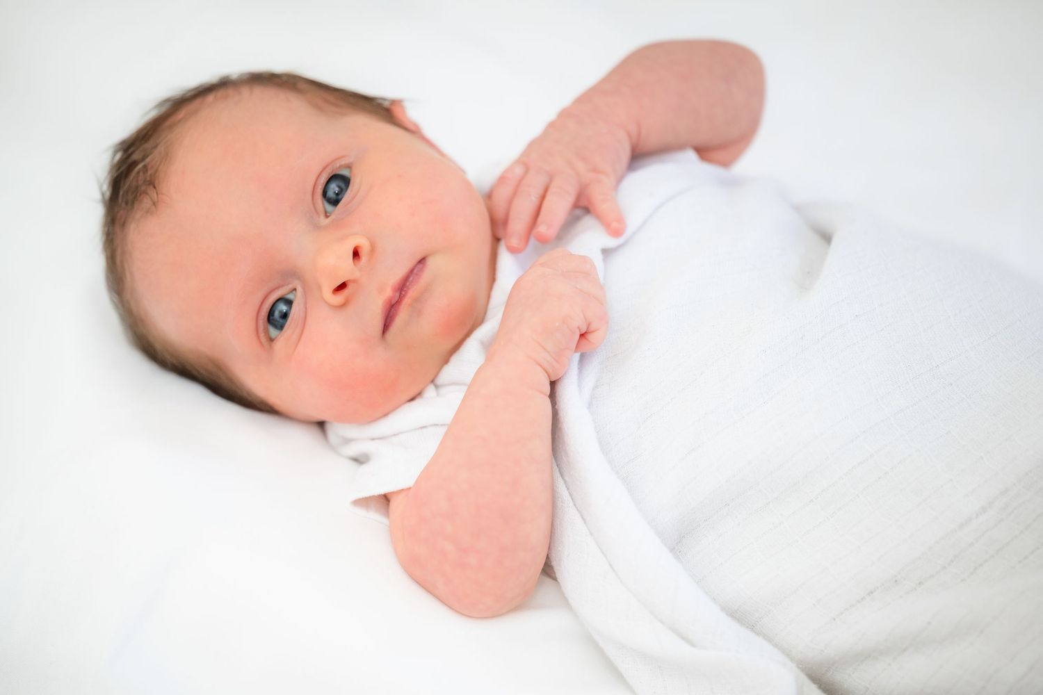 A series of four close-up shots showing a newborn baby in white swaddling against a light background.