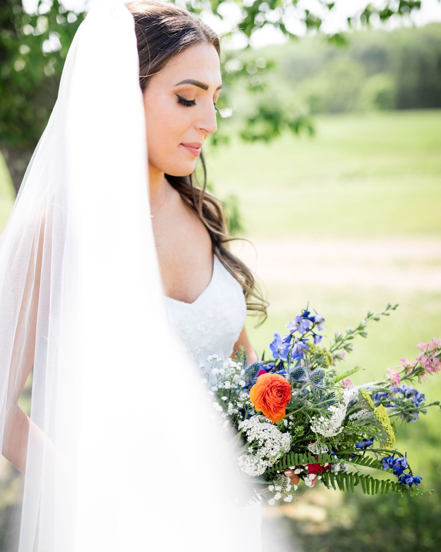 Profile view of a bride holding a vibrant bouquet of mixed wildflowers against a green landscape.