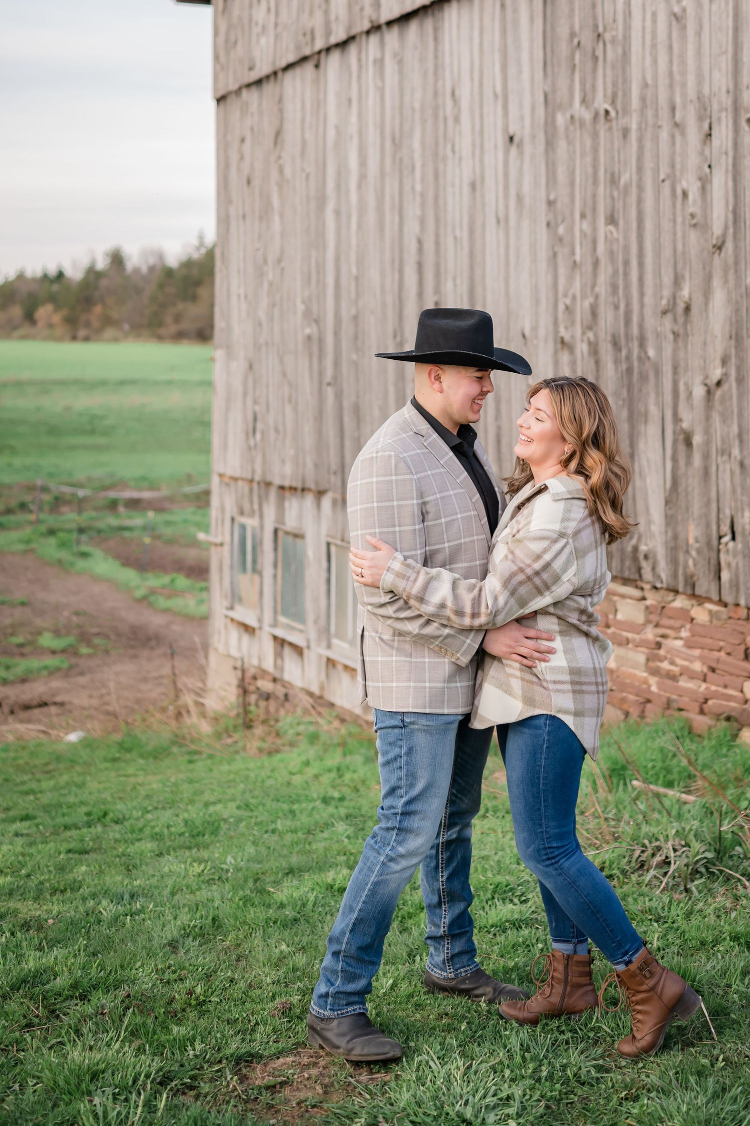 A couple shares a tender moment against a rustic wooden barn wall.