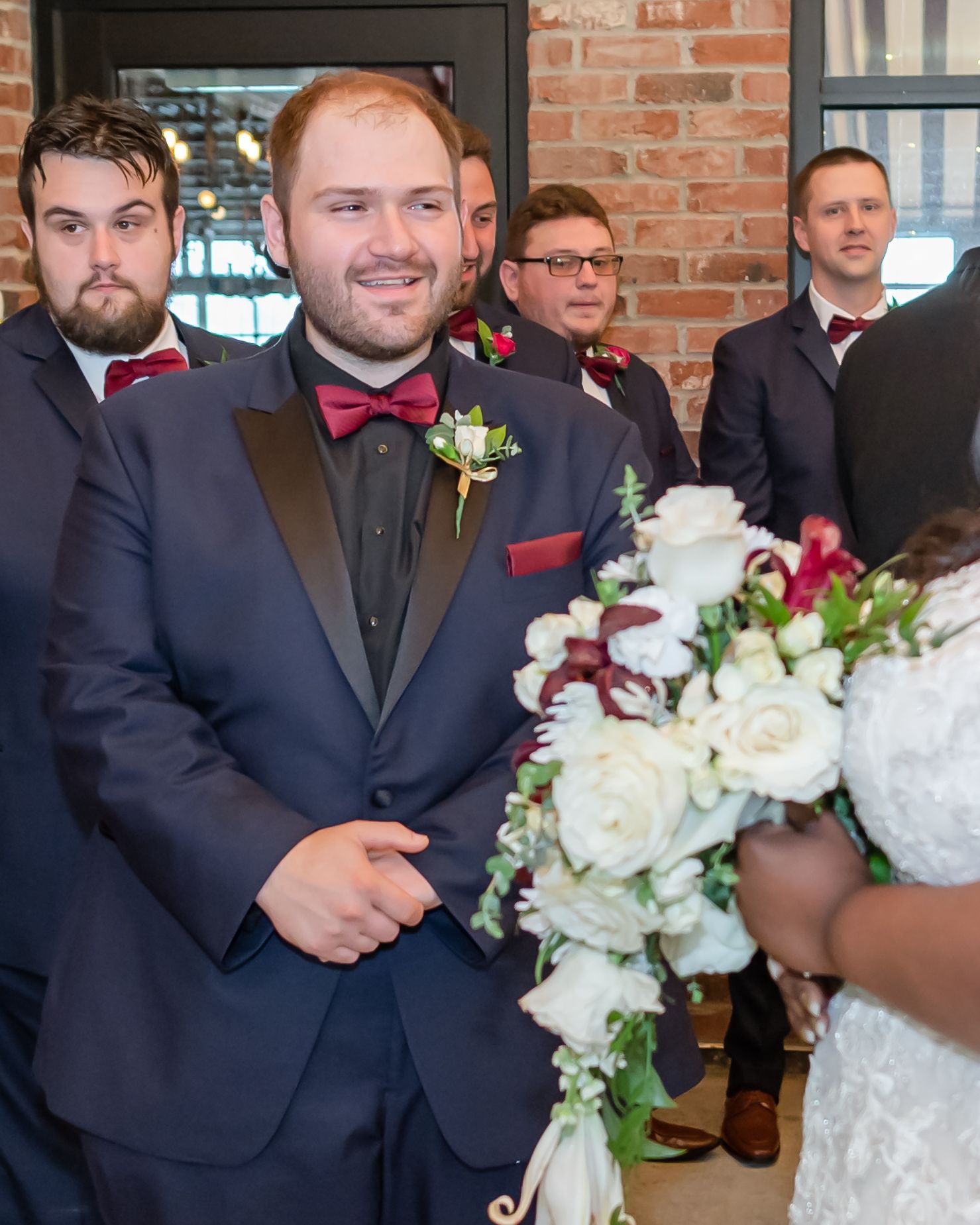Groomsmen in formal attire standing near white floral arrangements at the ceremony.