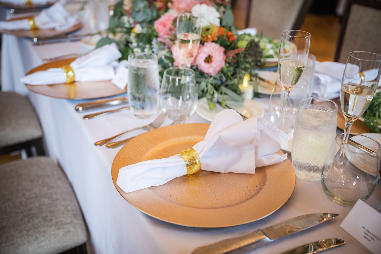 Elegant wedding table setting with gold charger plates and white linens.