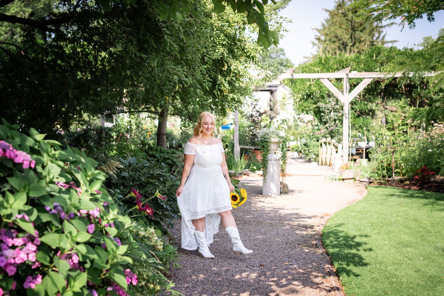 A bride walks along a garden path surrounded by blooming flowers and greenery.