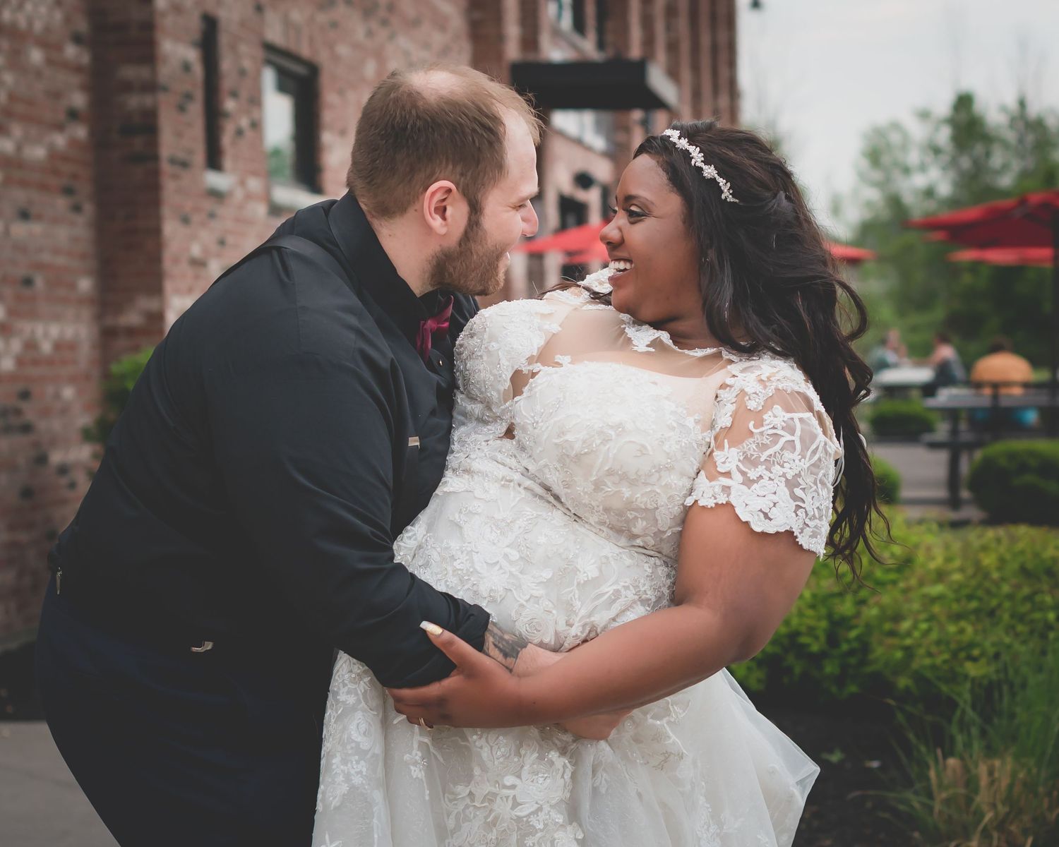 A romantic moment shared between newlyweds in their wedding attire outside a brick building.