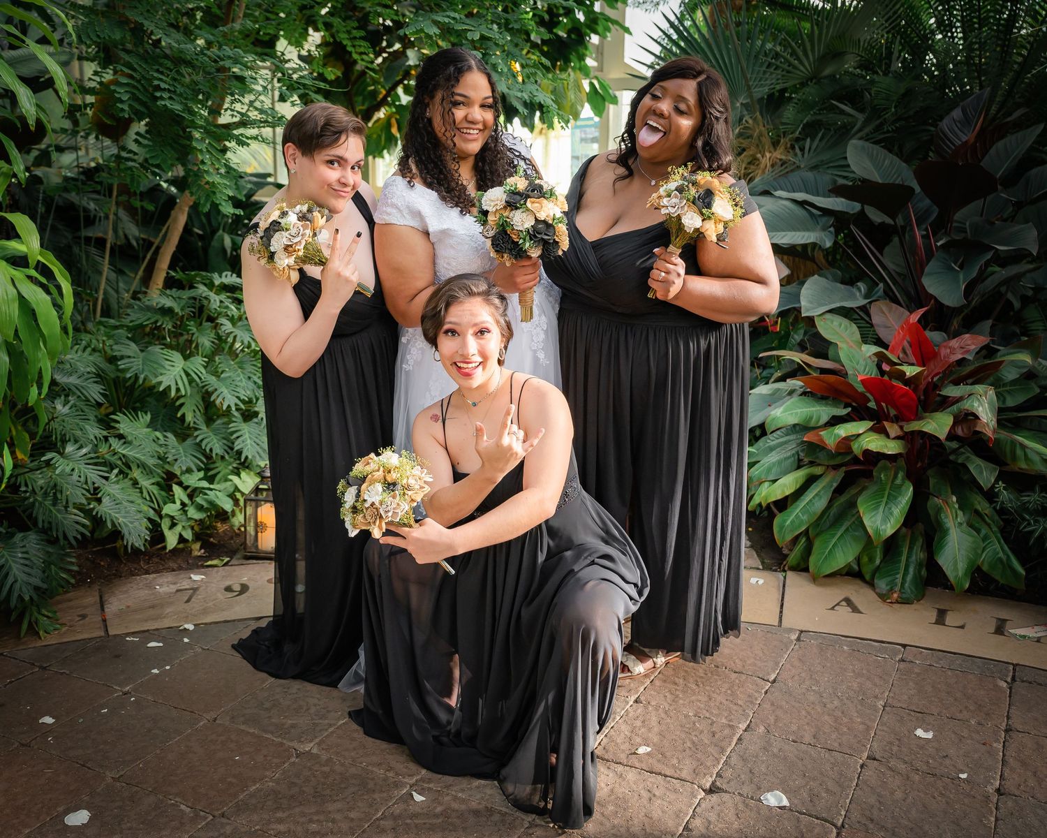 Wedding party in black dresses poses together against lush tropical garden backdrop.
