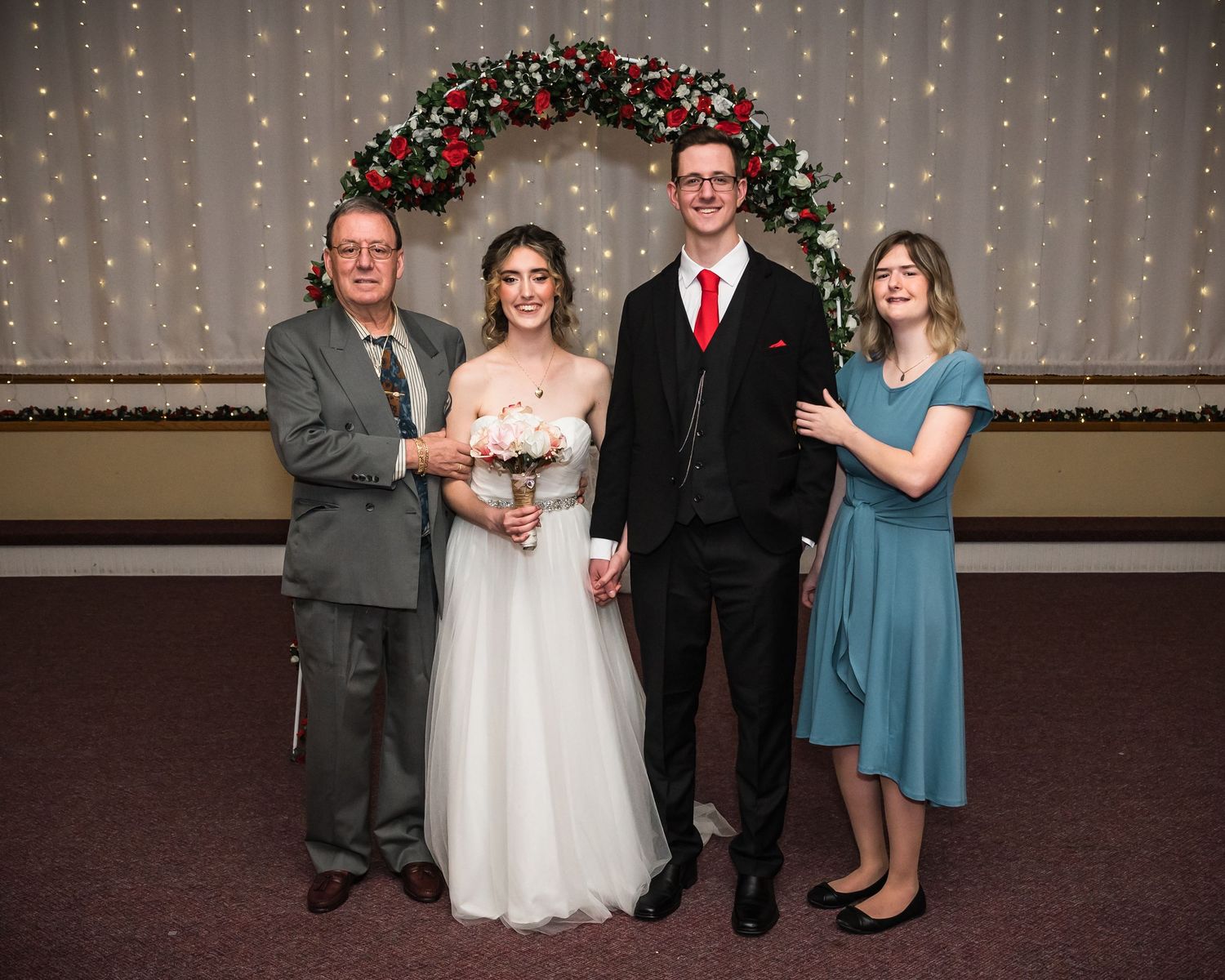 Small wedding group poses under a decorated holiday arch with twinkle lights.