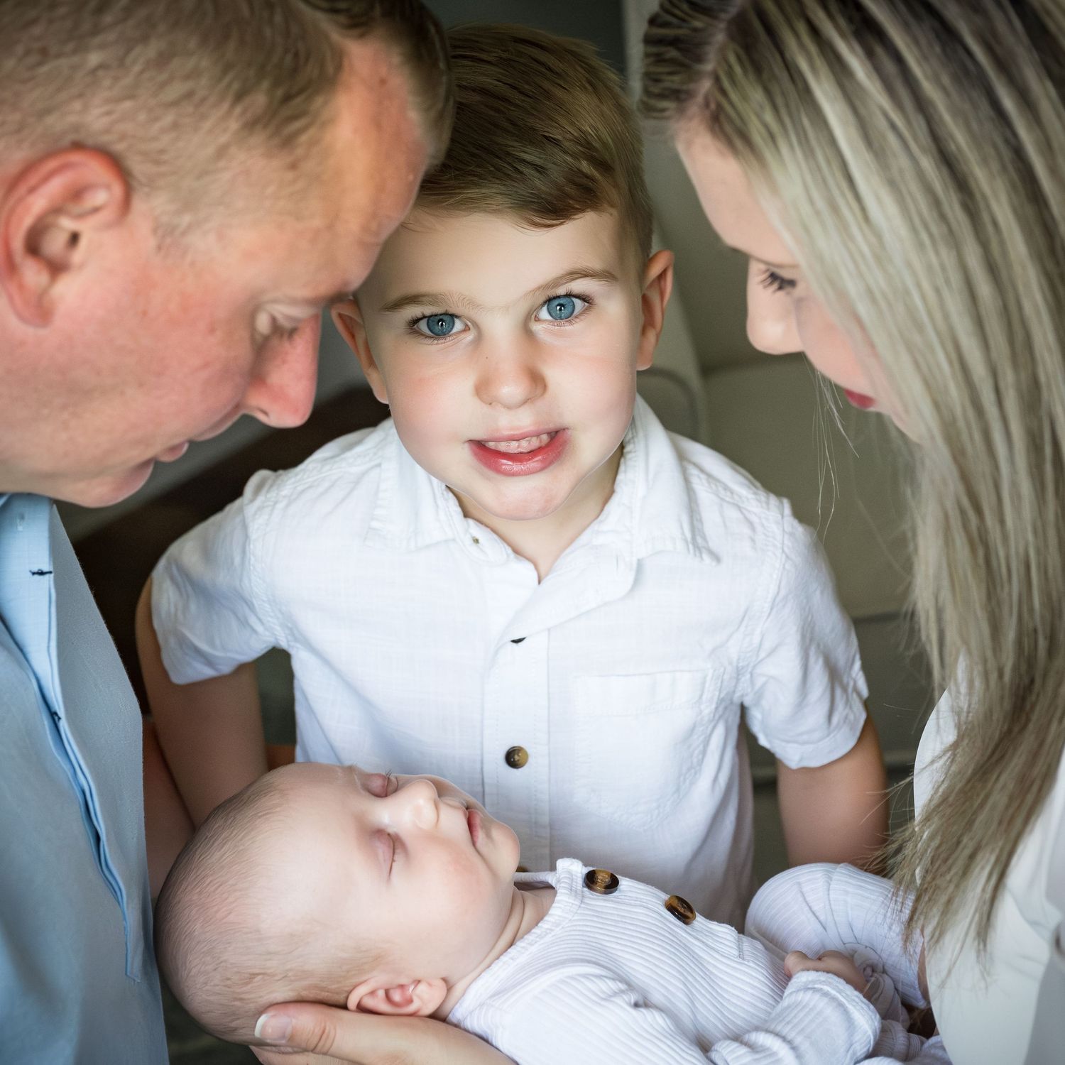 Family gathered close together looking at their newborn baby in an intimate indoor portrait.