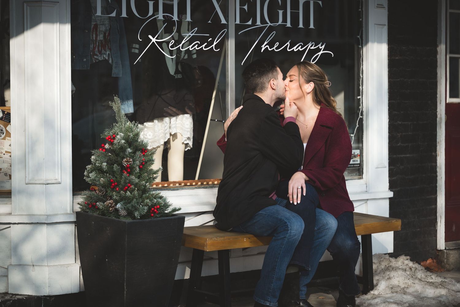 Couple sharing a romantic kiss on a bench outside Eight Eight Retail Therapy shop with Christmas decorations.