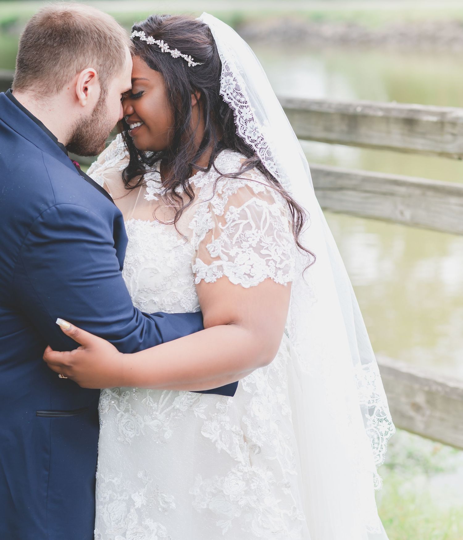 A romantic wedding couple shares an intimate moment together outdoors near a tranquil waterfront setting.